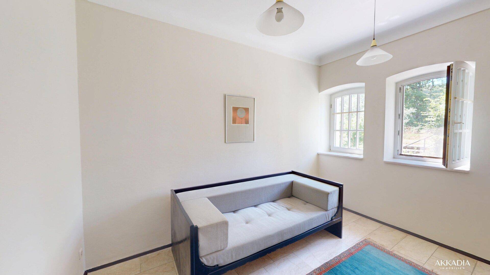 Helles Zimmer mit beigem Fliesenboden, zwei Fenstern und einem Tagesbett, ideal als Gästezimmer.