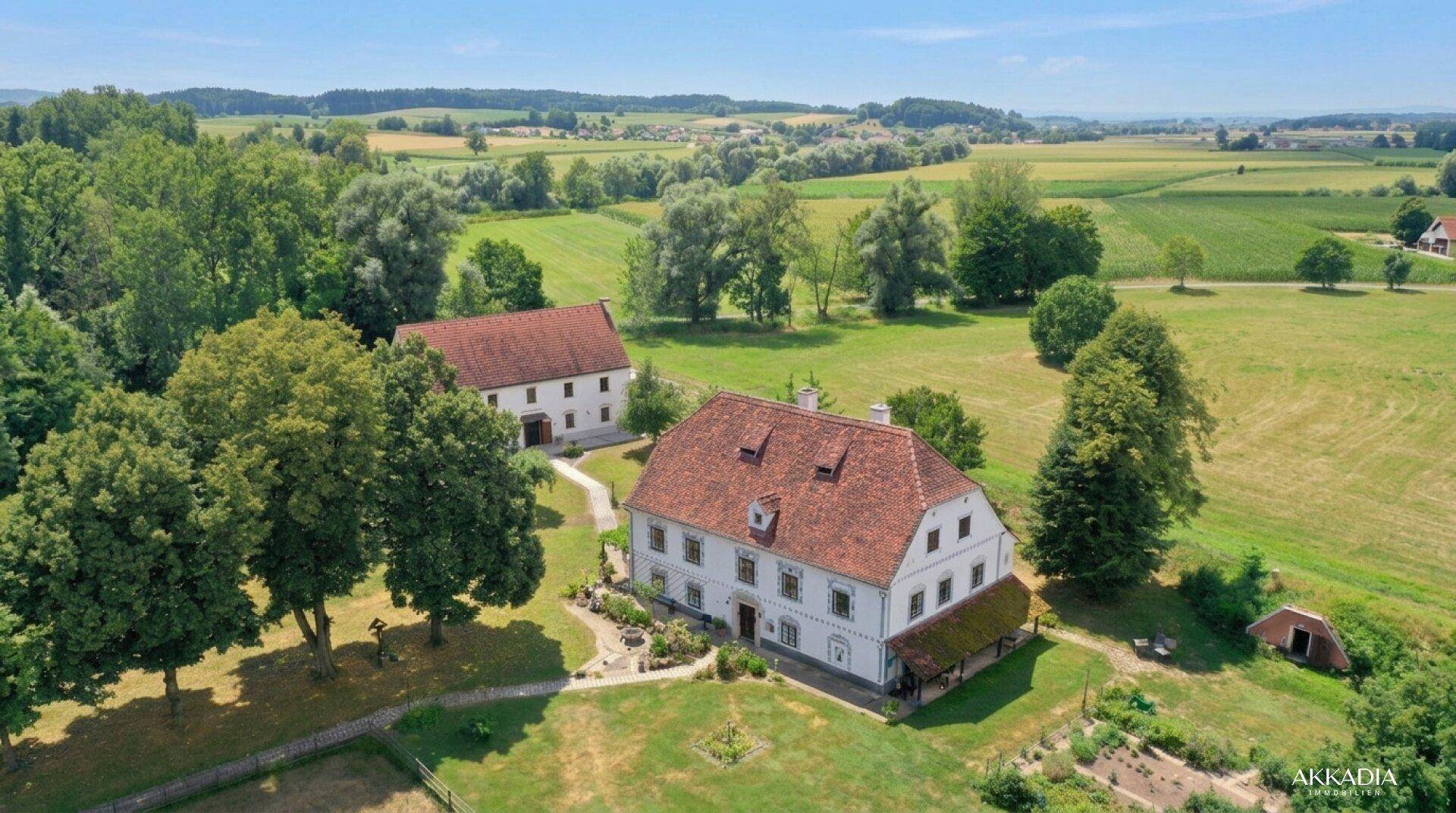 Weitläufiges Anwesen mit mehreren Gebäuden, umgeben von Feldern und Bäumen unter sonnigem Himmel.
