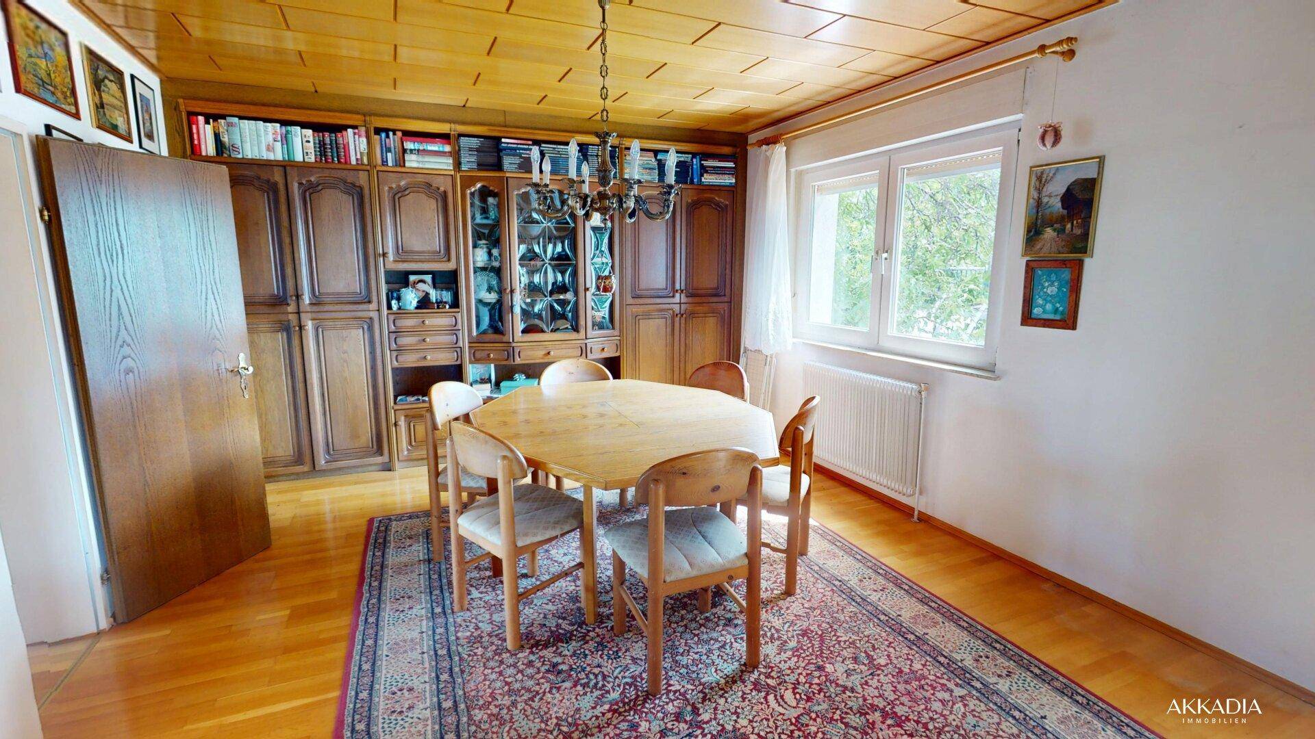 Traditionelles Esszimmer mit rundem Holztisch, passenden Stühlen und einem großen Bücherregal unter Holzdecke.