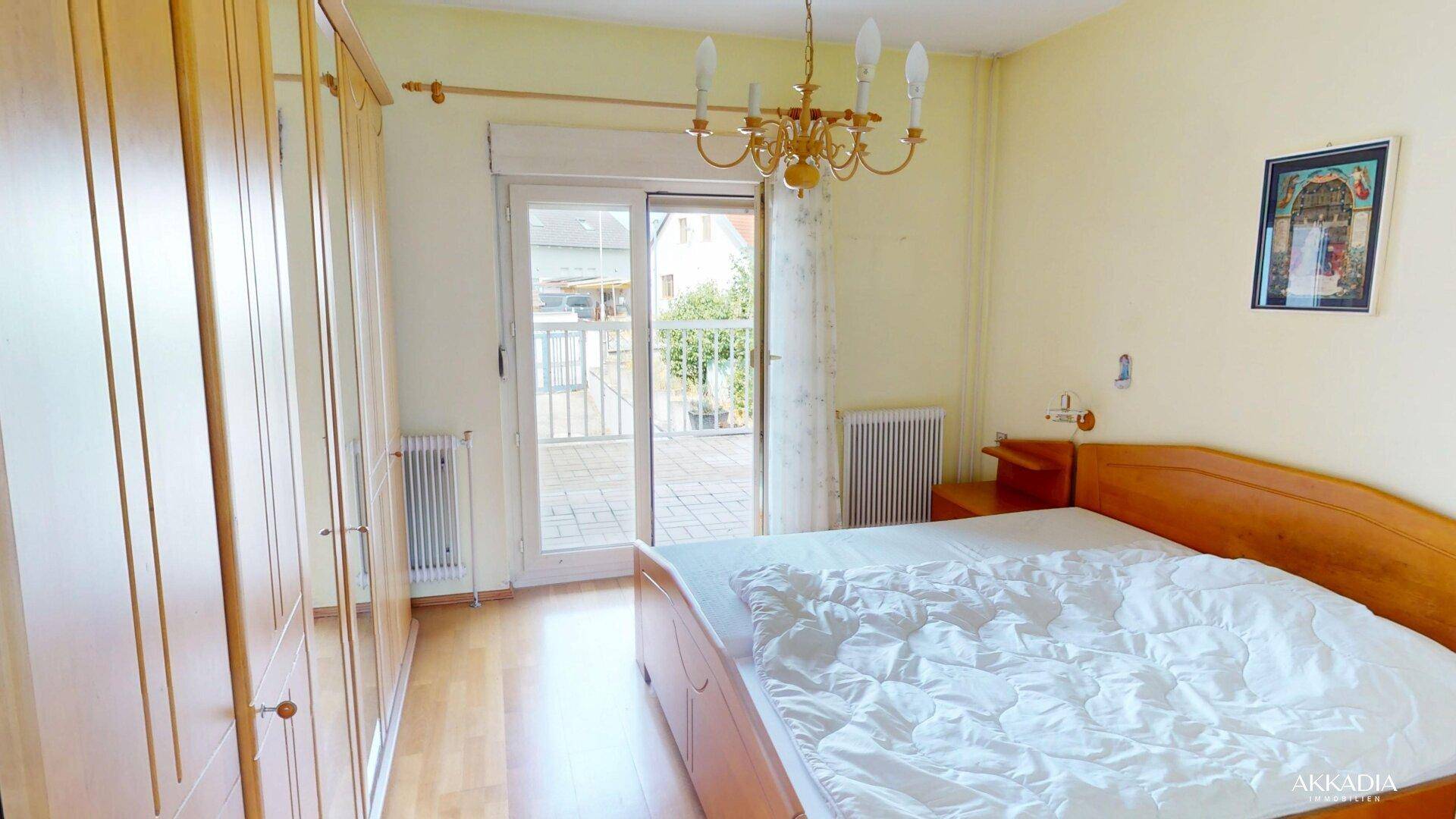 Schlafzimmer mit Holzbett, großem Kleiderschrank und direktem Zugang zu einem sonnigen Balkon.