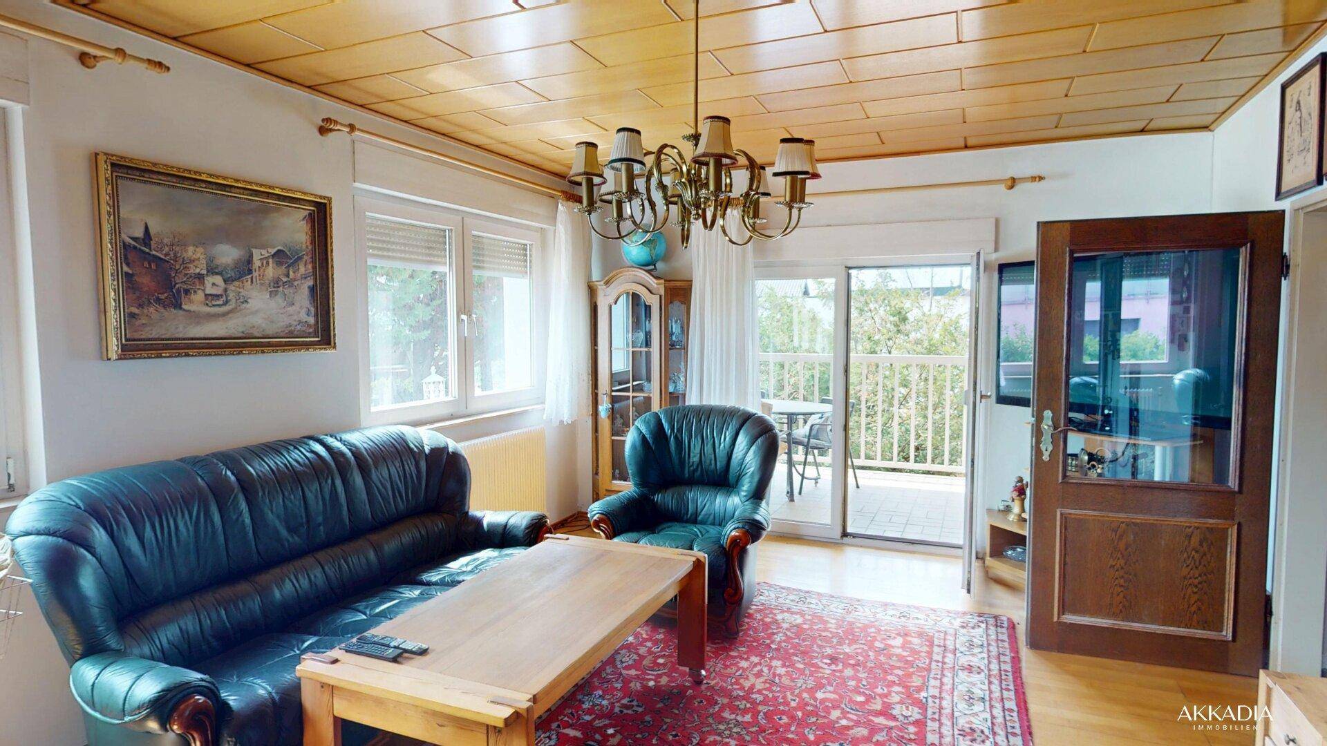 Gemütliches Wohnzimmer mit dunklem Ledersofa, Holztisch und Zugang zu einem sonnigen Balkon.