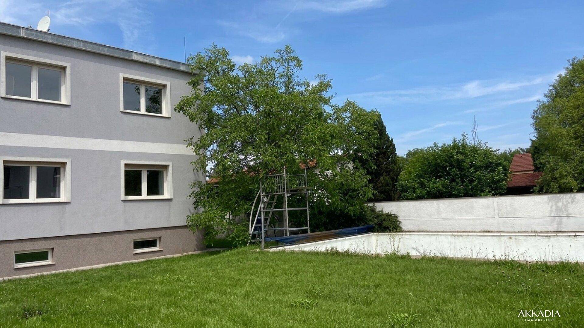 Seitenansicht des Gebäudes mit einem grünen Rasen, einem Baum und einer Betonmauer im Gartenbereich.