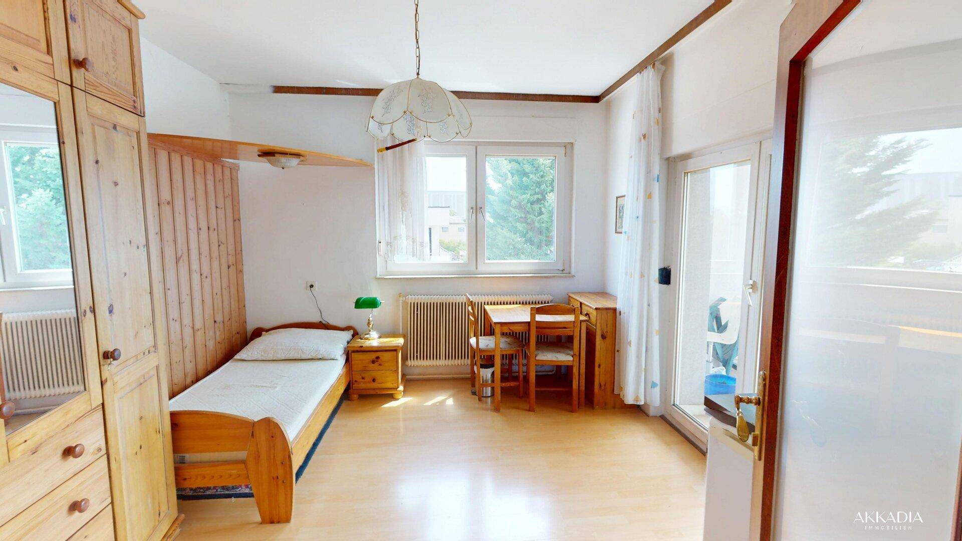 Schlafzimmer mit Einzelbett, Holzschrank, kleinem Esstisch und direktem Zugang zum Balkon.