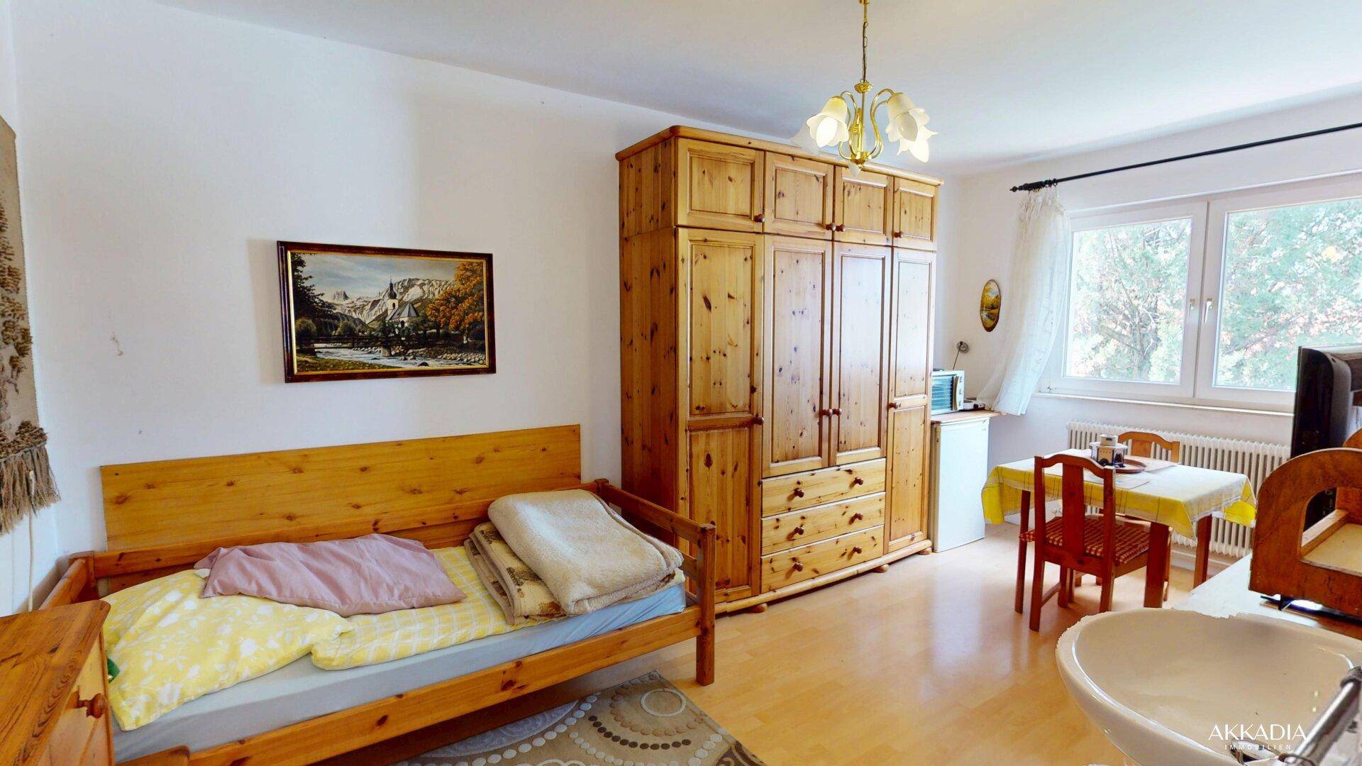 Schlafzimmer mit Einzelbett, großem Holzschrank, kleinem Esstisch und integriertem Waschbecken.