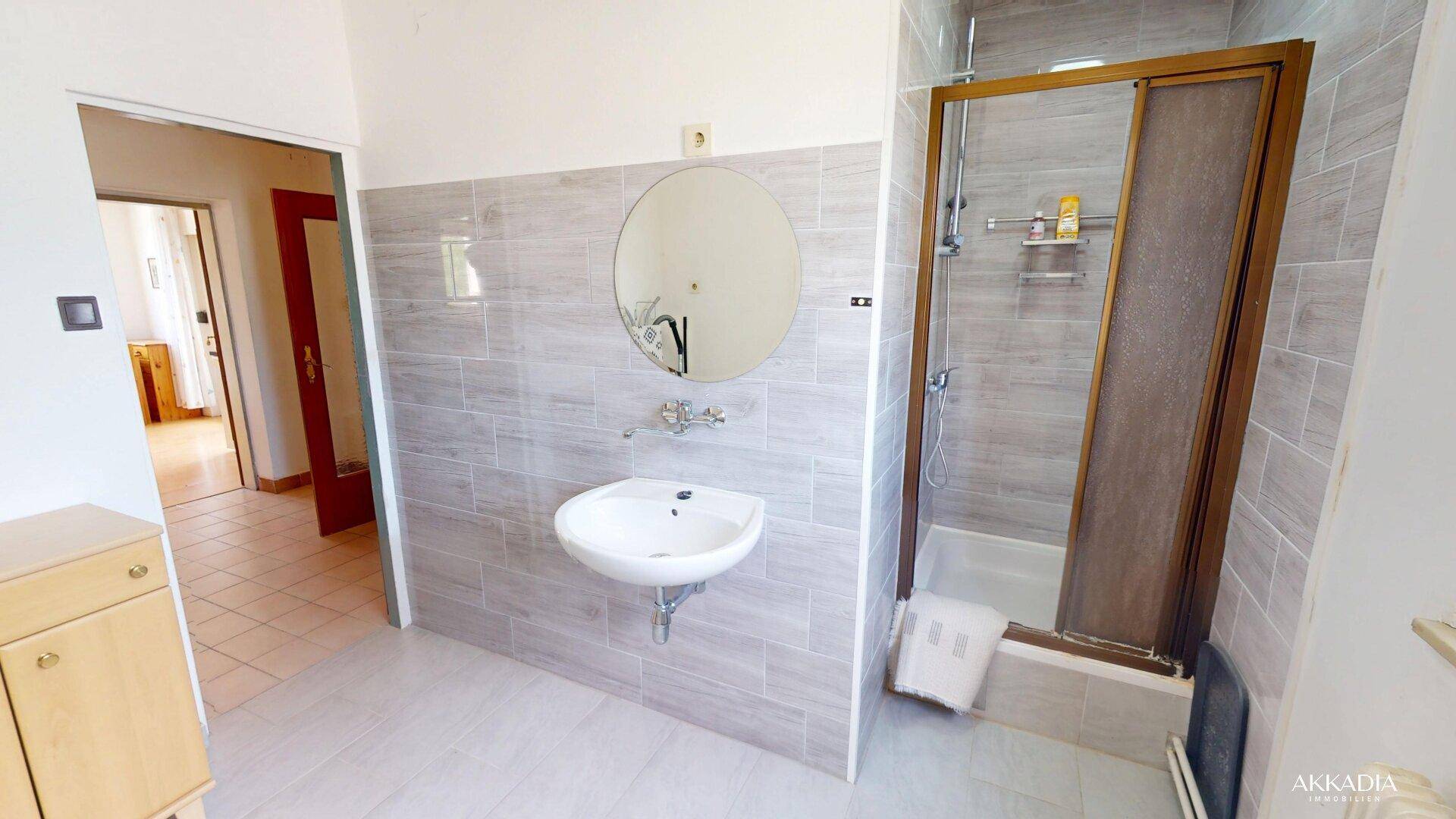 Badezimmer mit Duschkabine, Einzelwaschbecken und einem runden Spiegel über dem Waschtisch.