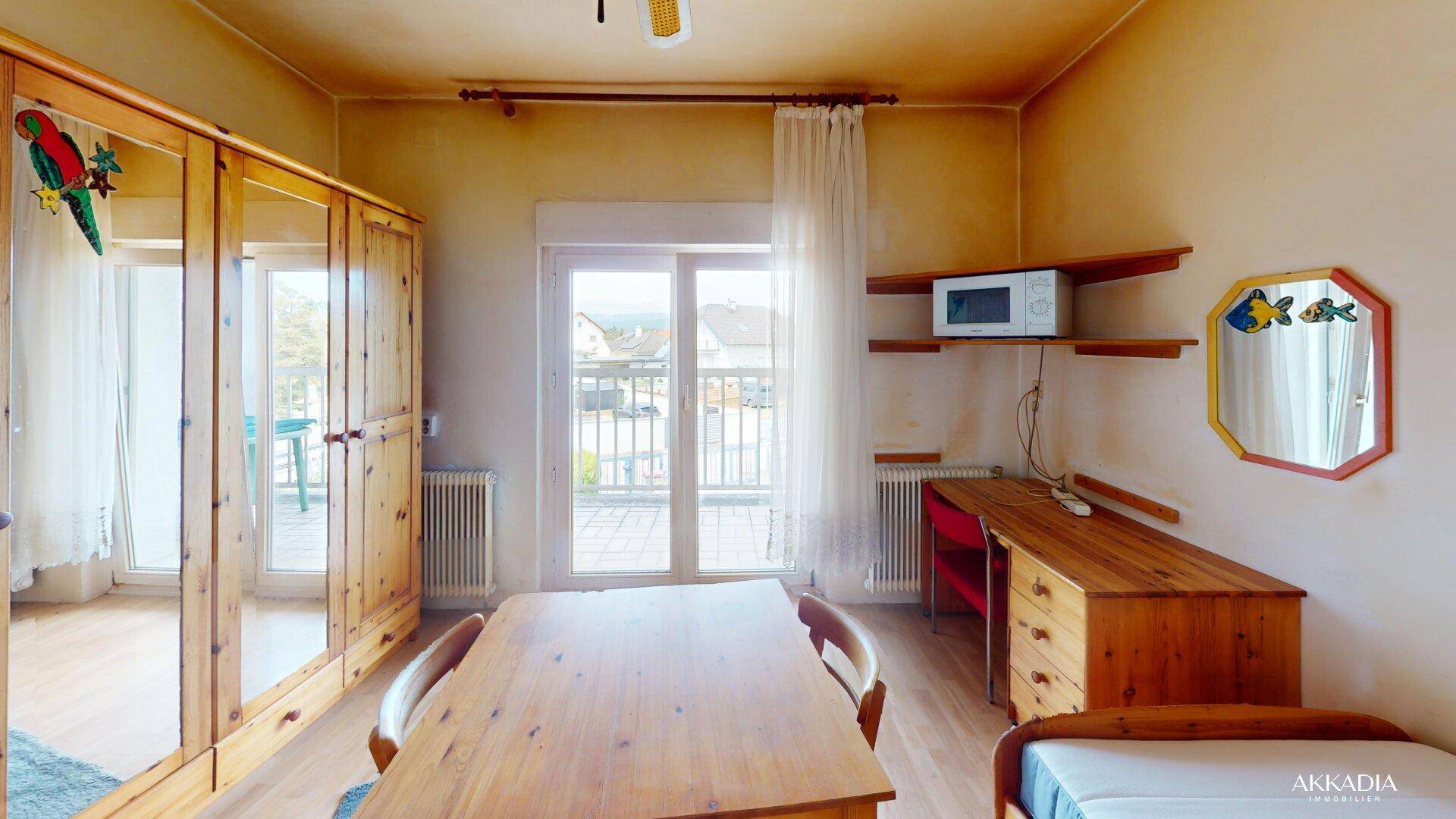 Geräumiges Schlafzimmer mit großem Holzschrank, Esstisch und Balkonzugang.