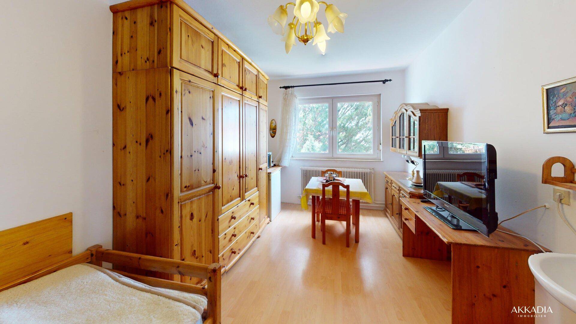 Helles Schlafzimmer mit großem Holzschrank, Fernseher und einem kleinen Essbereich.