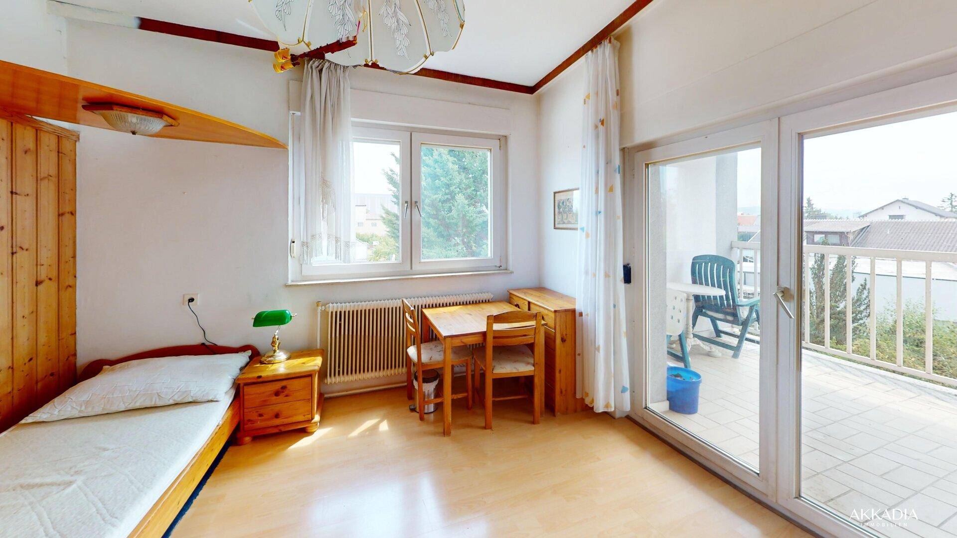 Helles Schlafzimmer mit Balkonzugang, Einzelbett und einem kleinen Essbereich.