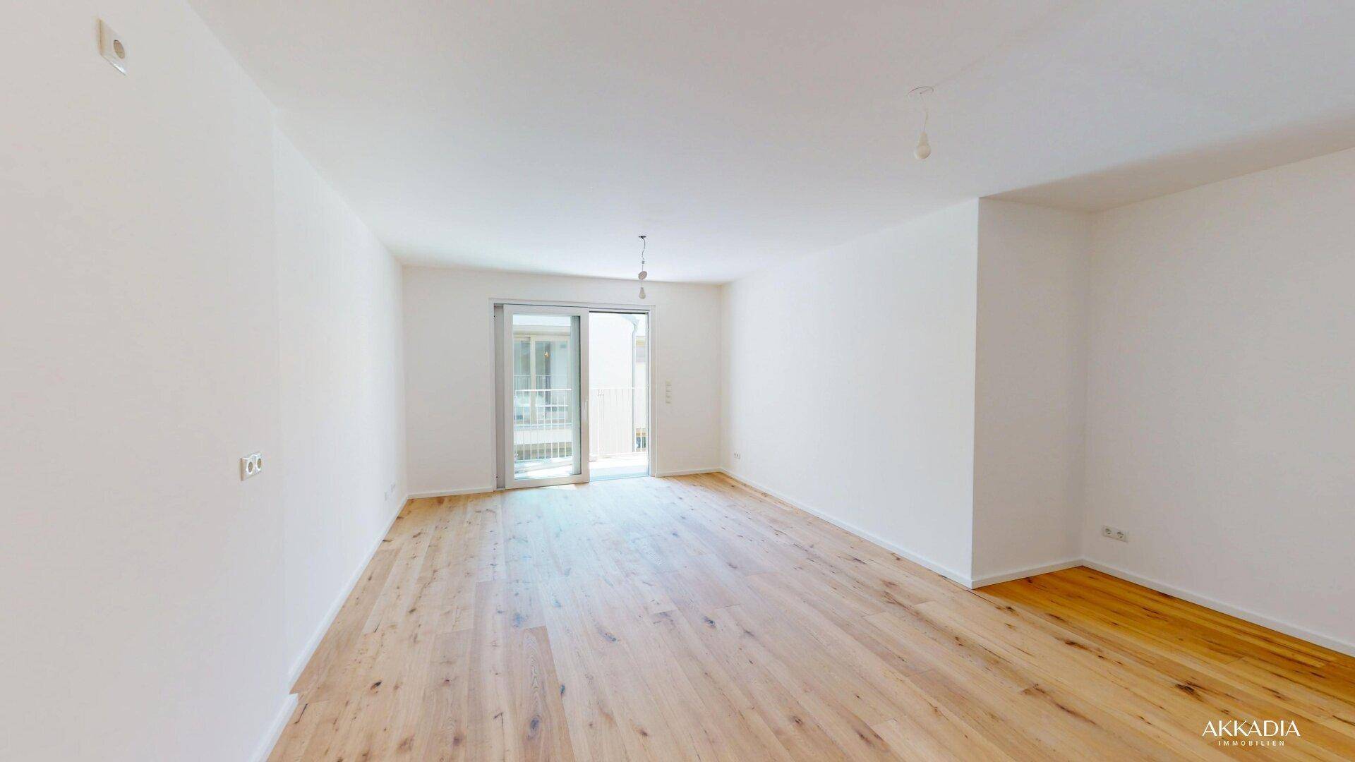 Heller Raum mit Holzboden und Zugang zu einem Balkon oder einer Terrasse.