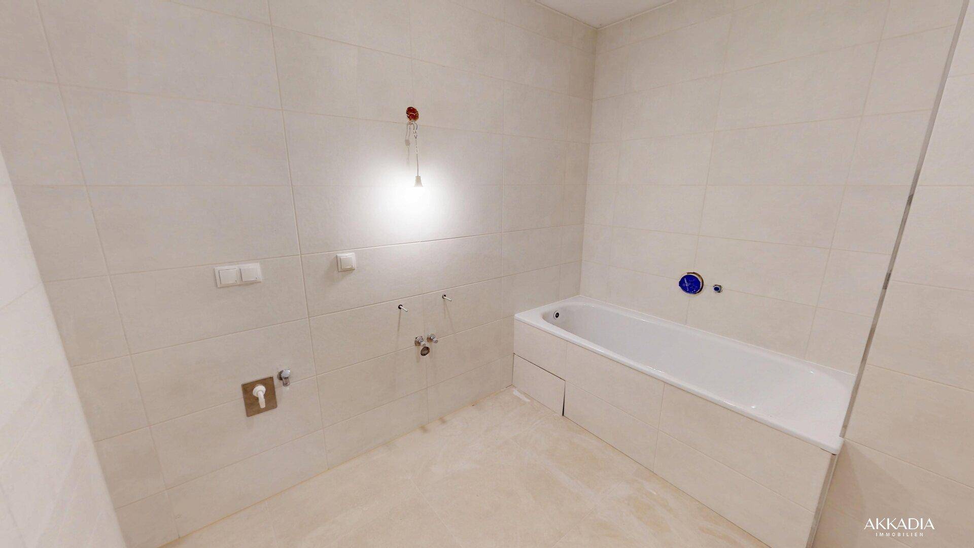 Unfertiges Badezimmer mit eingebauter Badewanne und hellen Fliesen an den Wänden.