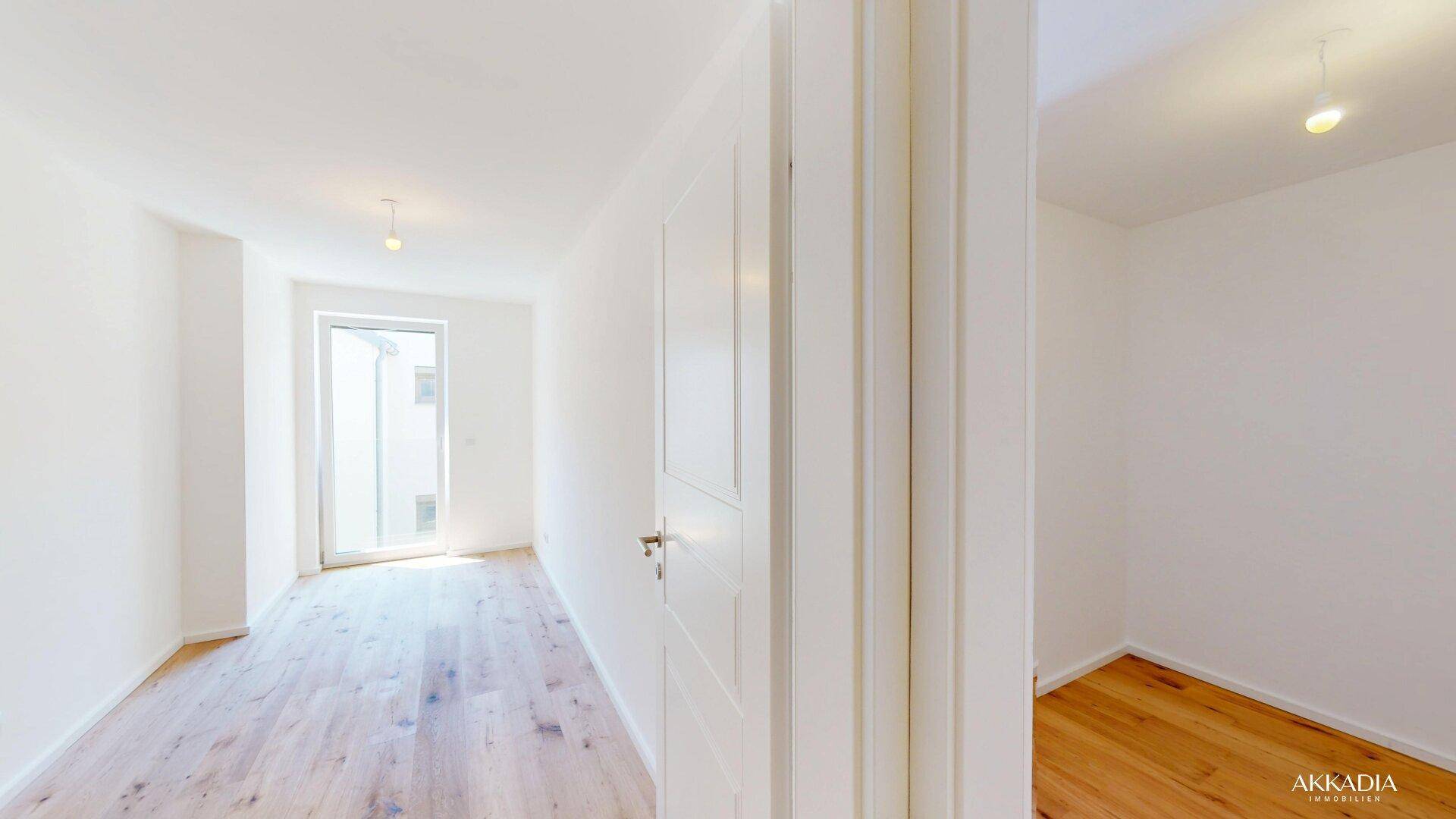 Heller Raum mit Holzboden und einer Tür, die zu einem weiteren Bereich des Apartments führt.