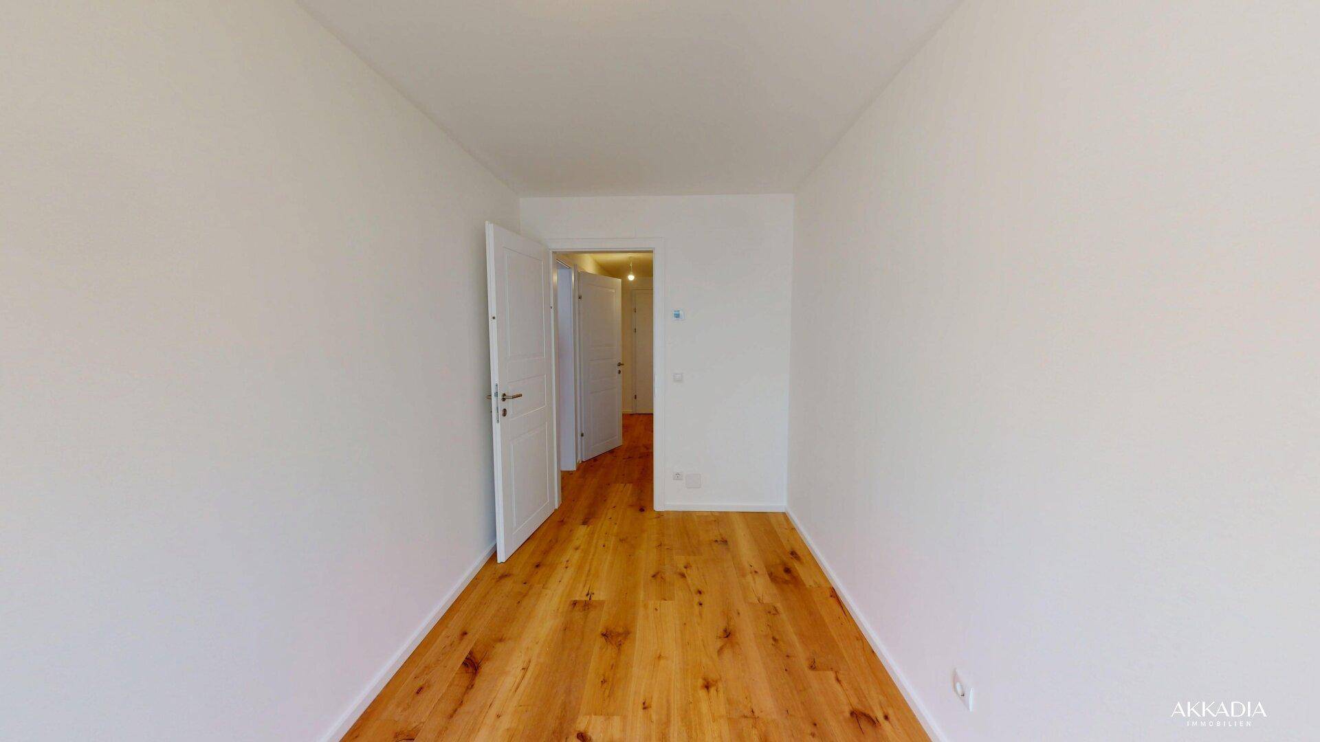 Geräumiger, heller Raum mit Holzboden und offener Tür, die den Blick in den Flur freigibt.