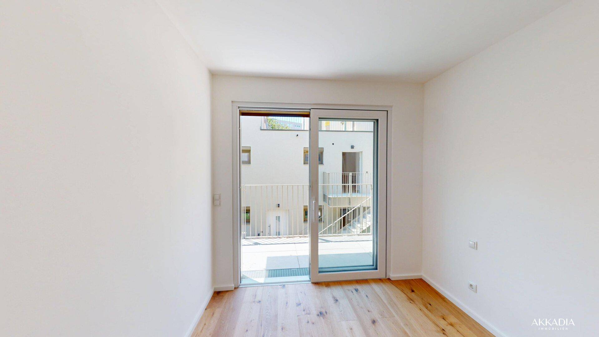 Heller Wohnraum mit Holzboden und großer Glasschiebetür, die den Zugang zum Außenbereich ermöglicht.