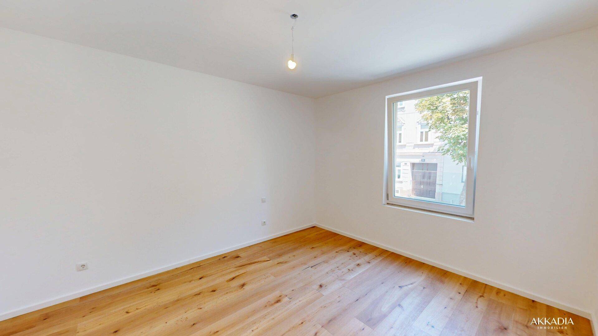 Geräumiges Zimmer mit hellem Holzboden und großem Fenster, ideal als Schlafzimmer.
