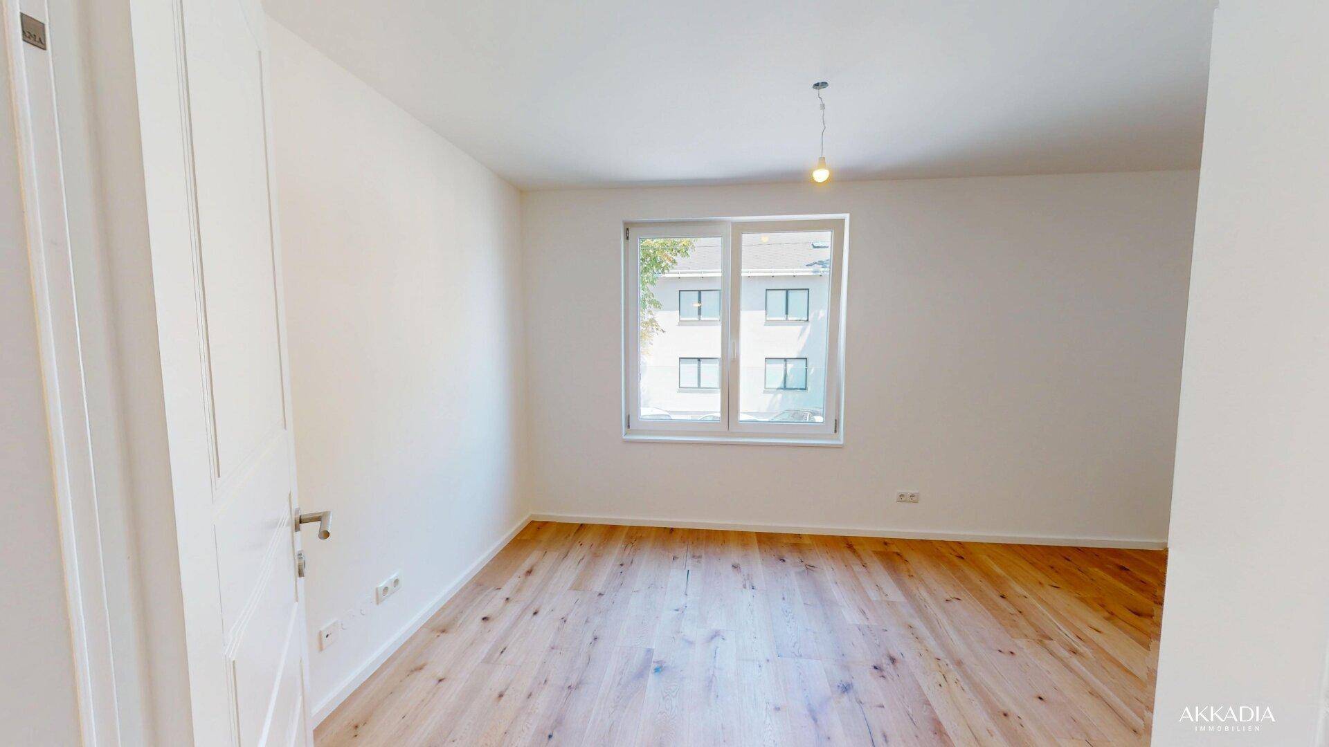 Geräumiges und helles Zimmer mit Holzboden und Blick nach draußen.