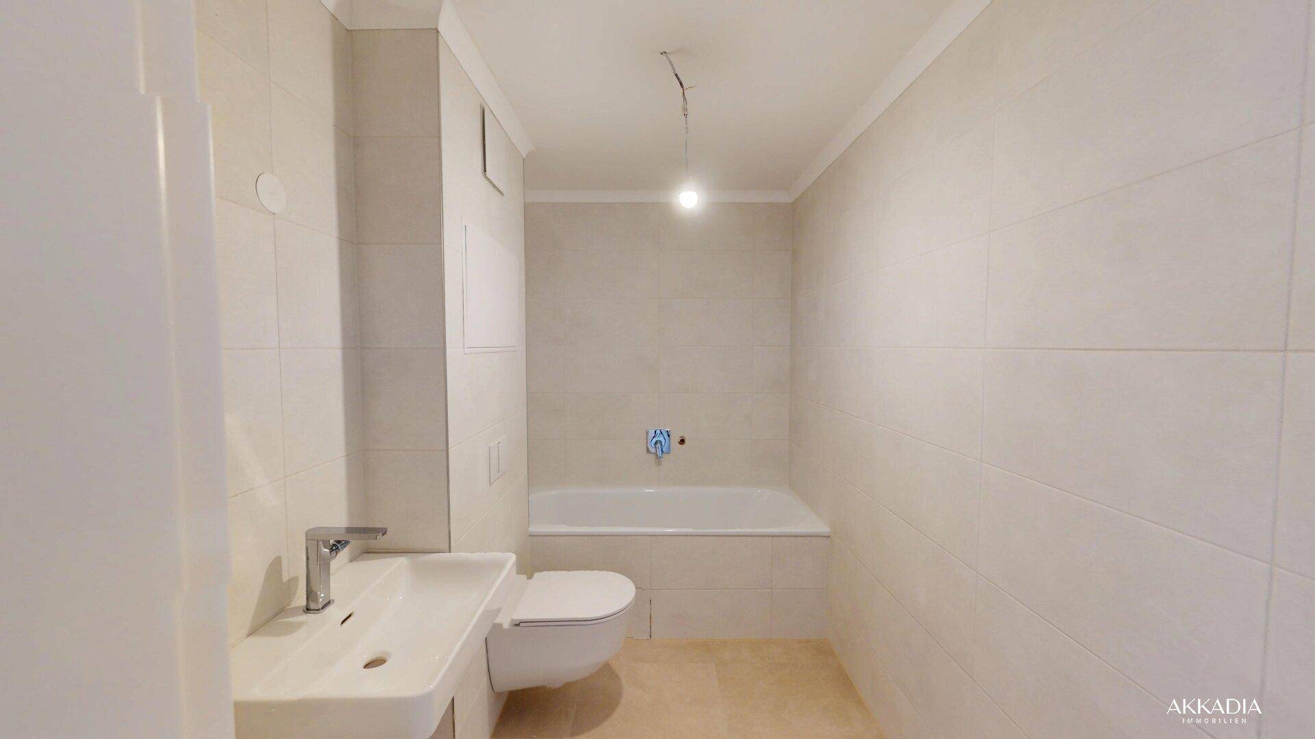 Modernes Badezimmer mit Badewanne, WC und Waschbecken, hell gefliest.