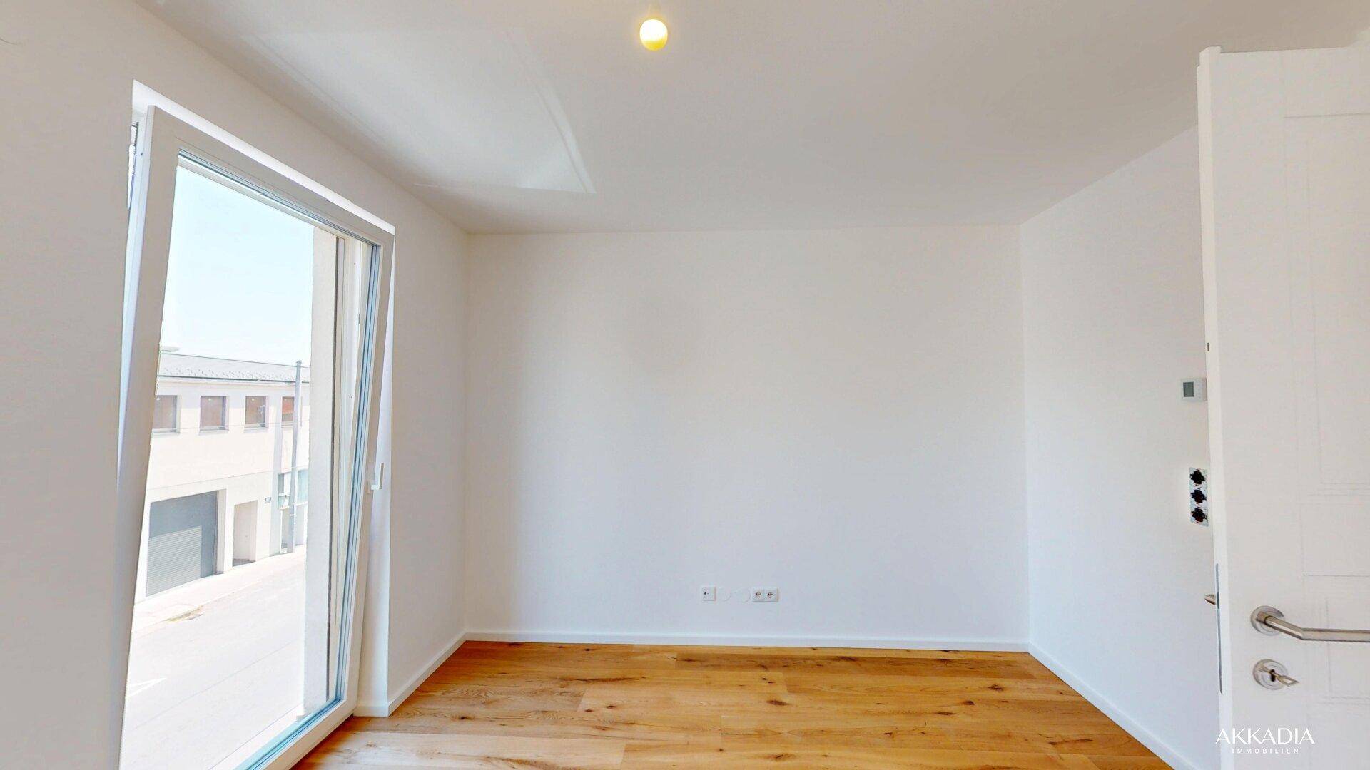 Leerer Raum mit Holzboden und einer Tür, die zu einem Balkon oder einer Terrasse führt.