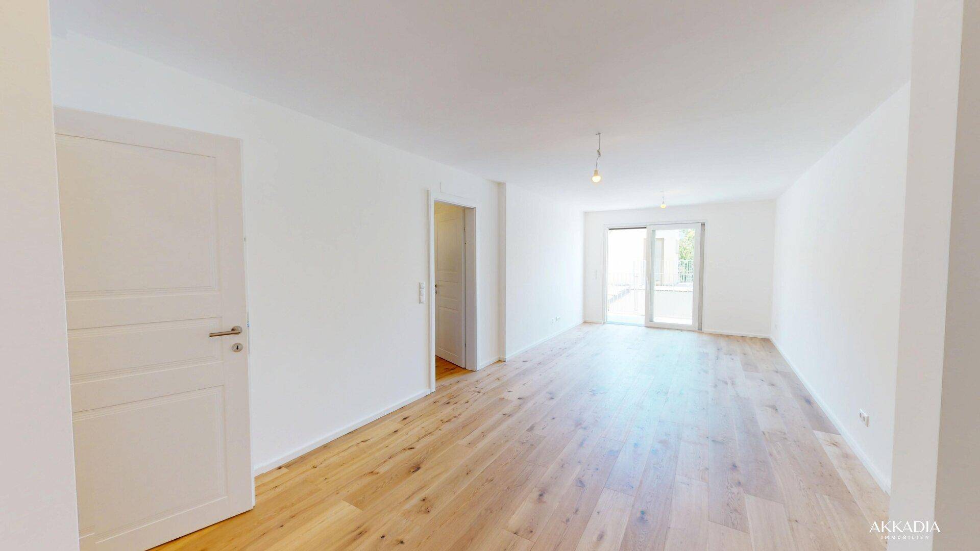 Helles, leeres Wohnzimmer mit Eichenparkettboden und Zugang zu einem Außenbereich.
