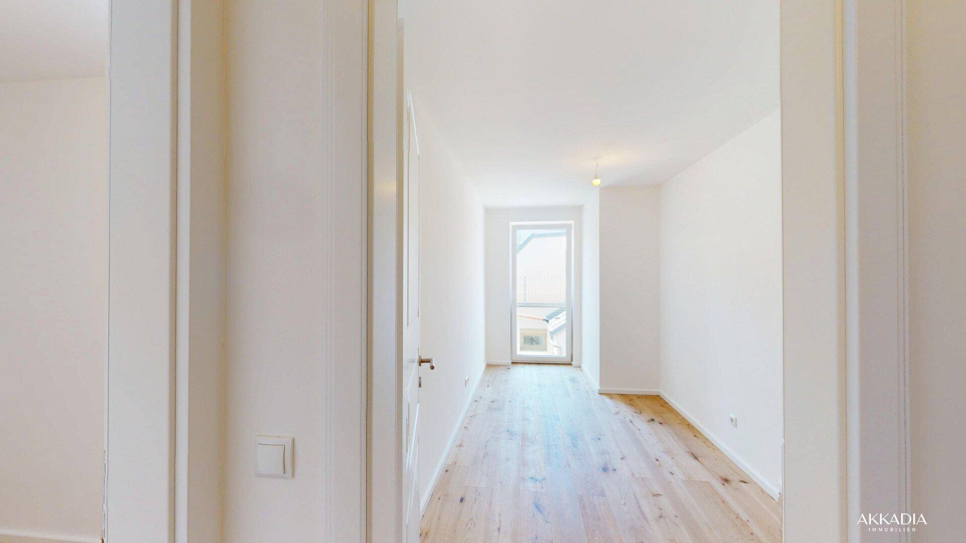 Heller Flur mit Holzboden und weiß gestrichenen Wänden, der zu einem Außenbereich führt.