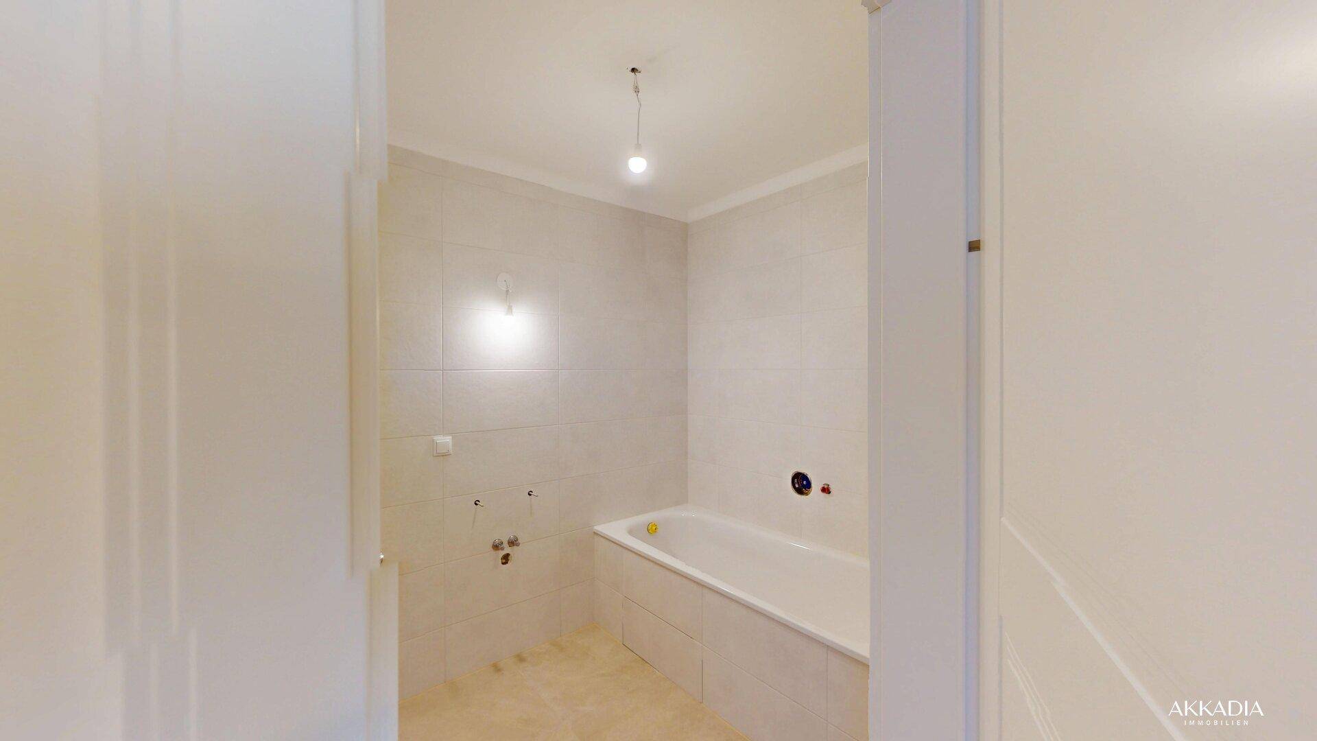 Unfertiges Badezimmer mit hellen Fliesen, eingebauter Badewanne und sichtbaren Sanitäranschlüssen.