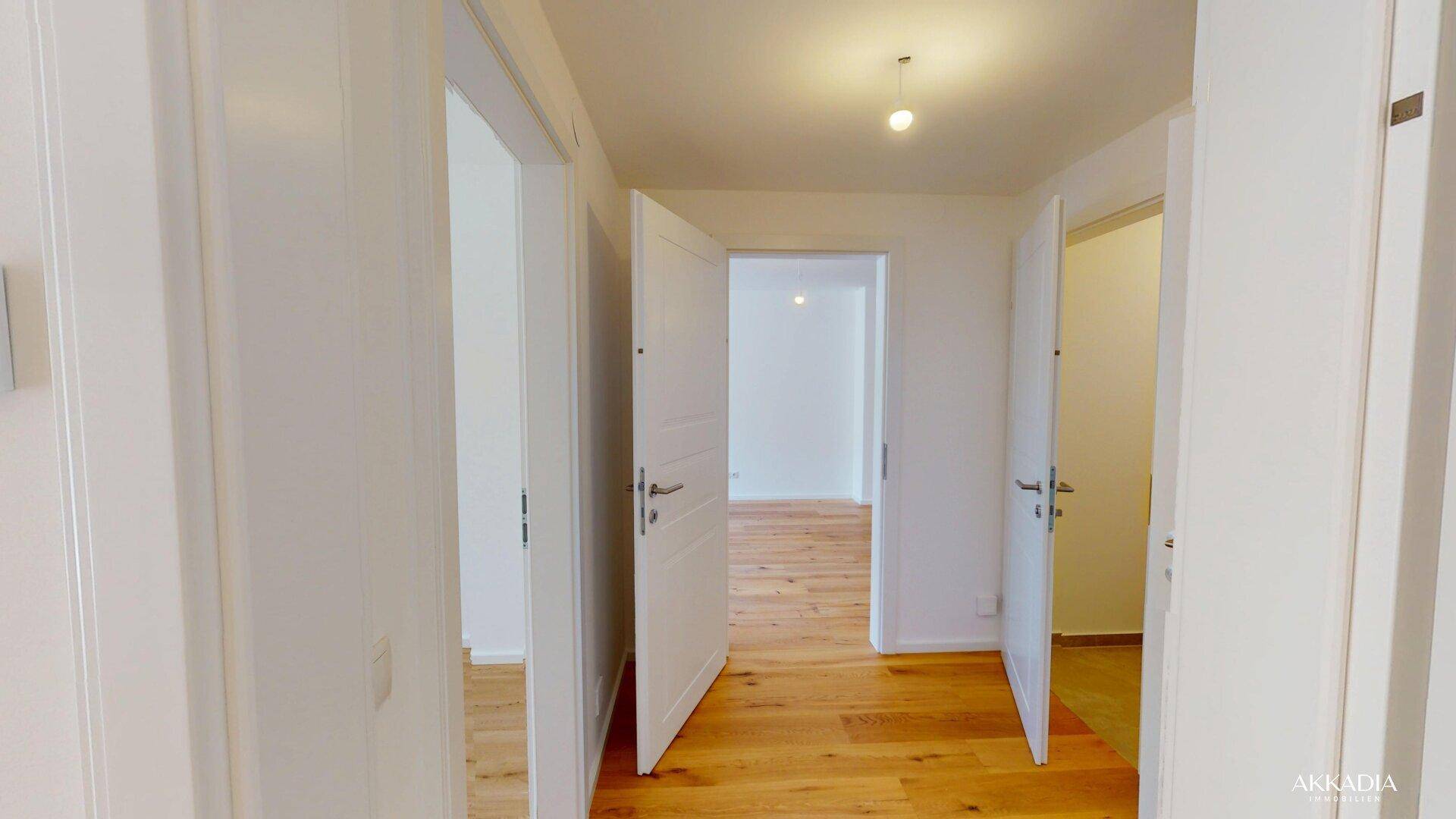 Heller Flur mit mehreren offenen weißen Türen und durchgehendem Holzboden.