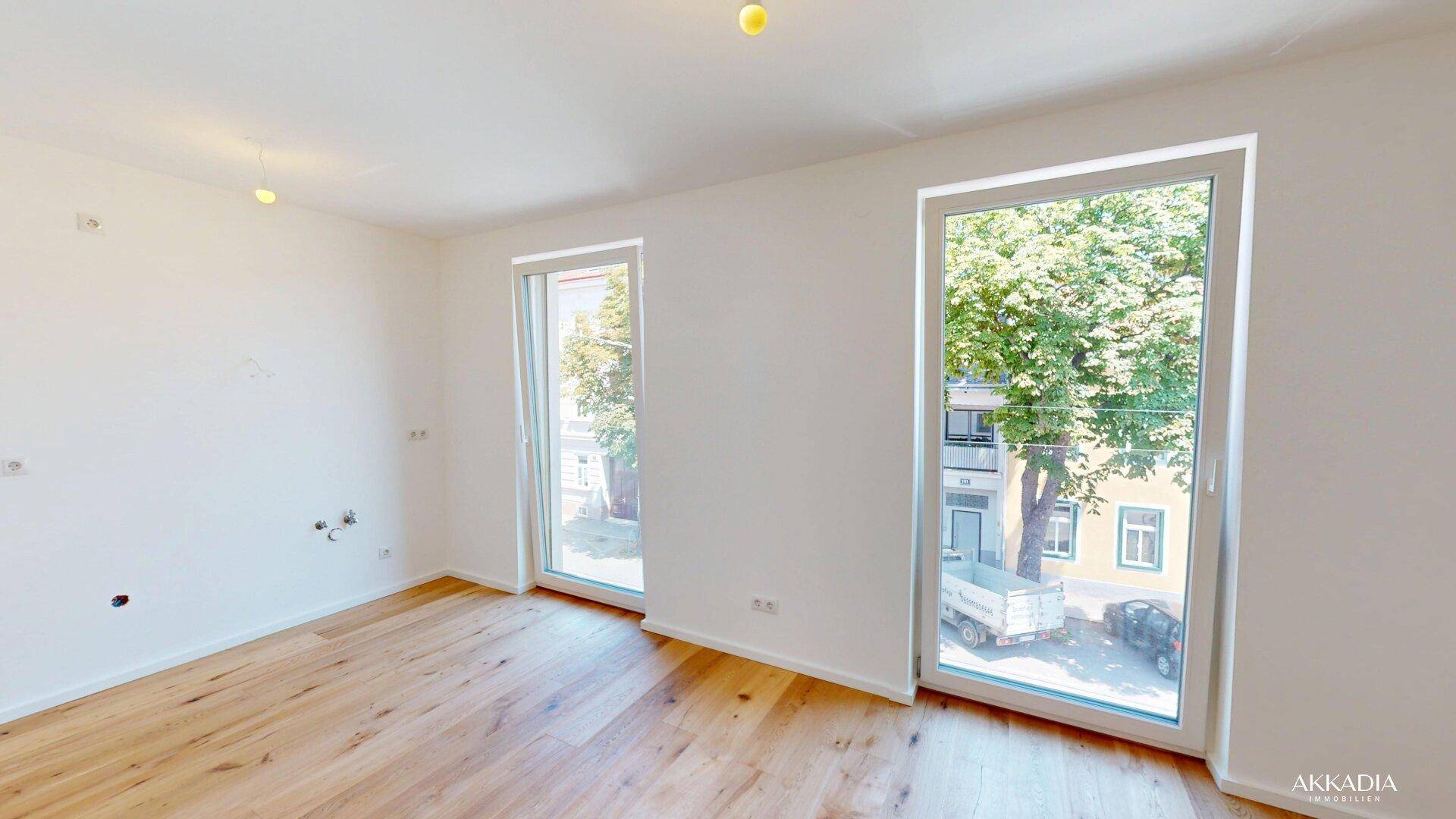 Lichtdurchfluteter Raum mit zwei hohen Fenstern und elegantem Holzboden.
