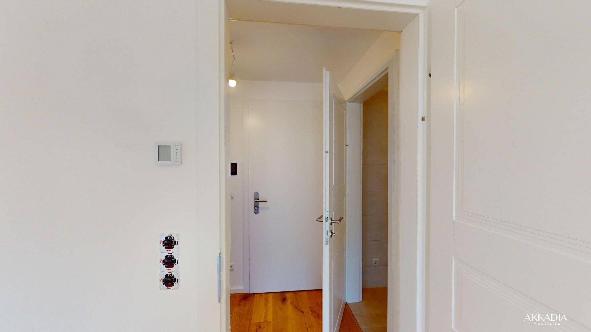Heller Flur mit weißen Türen, Holzboden und einem modernen Thermostat an der Wand.