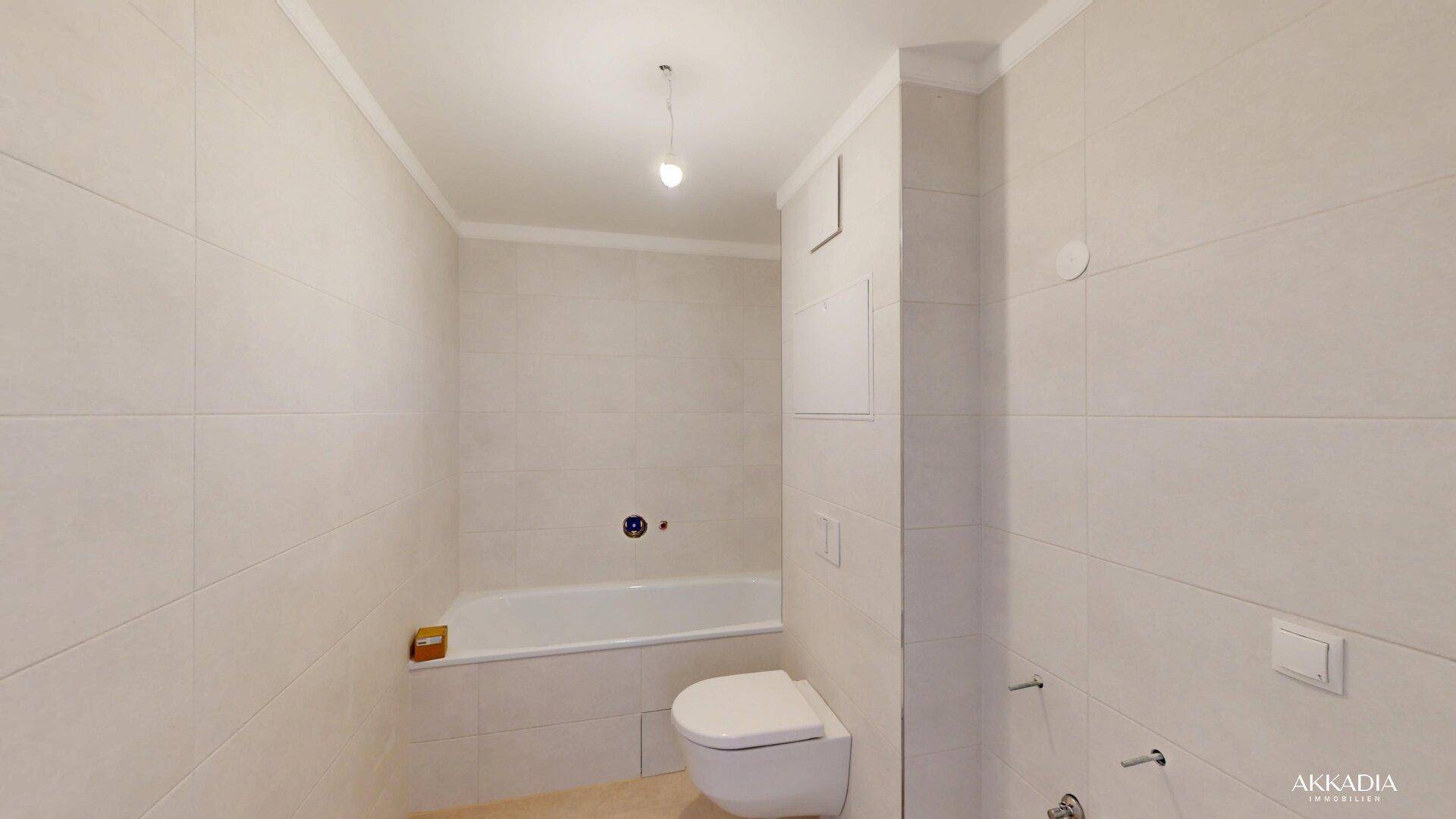 Modernes Badezimmer mit hellen Fliesen, Badewanne und wandhängendem WC.