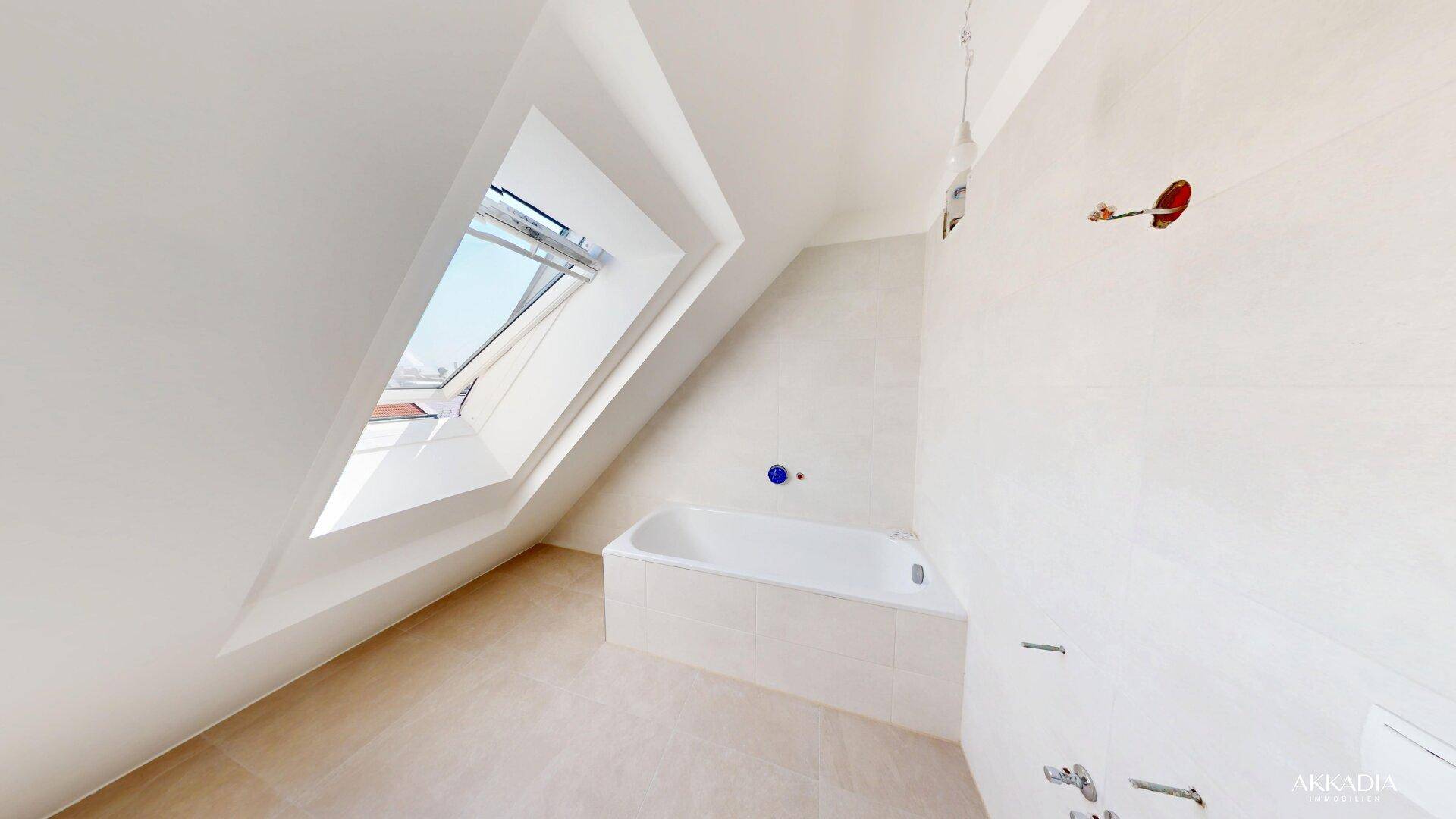 Modernes Badezimmer mit Badewanne, Fliesenboden und einem Dachfenster in der Dachschräge.