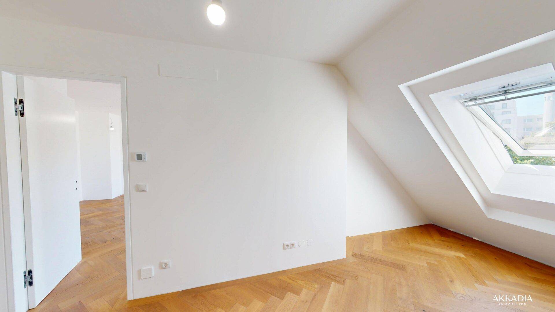 Helles Schlafzimmer mit Dachschräge, Fischgrätparkett und einem großen Dachfenster.