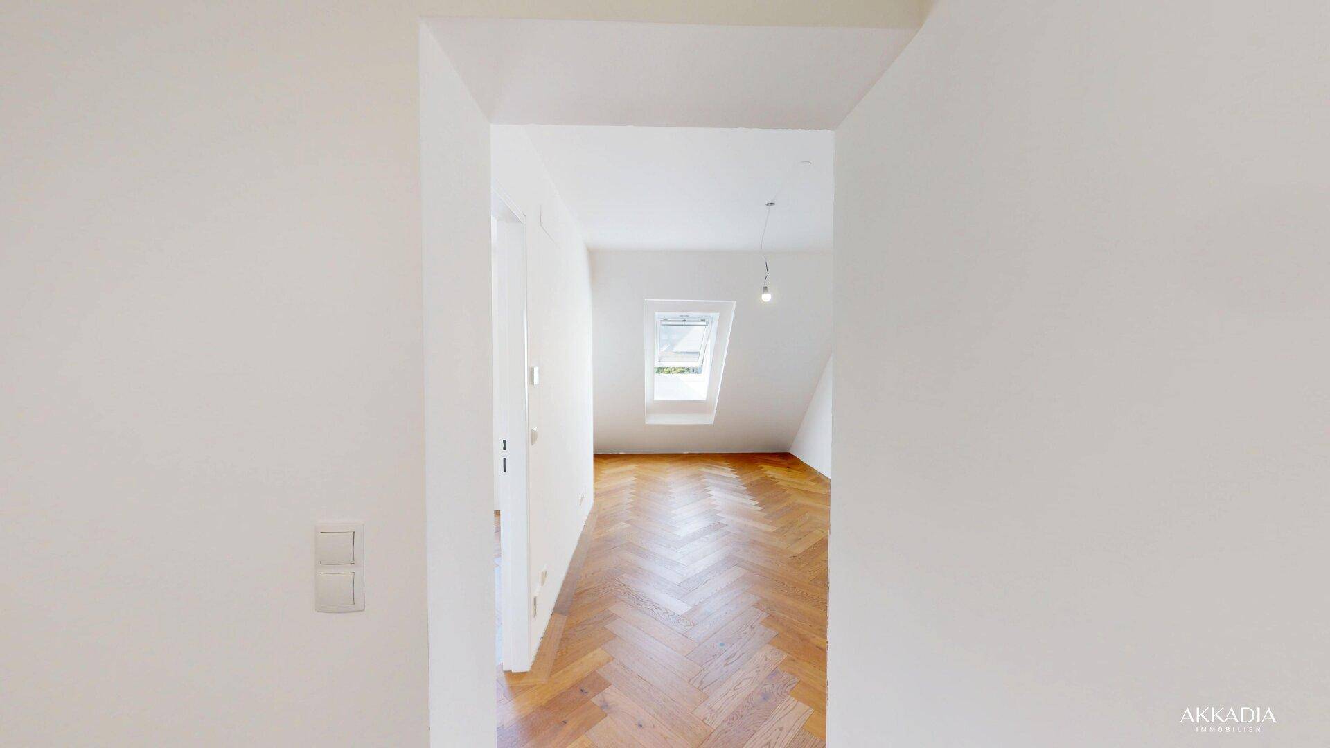 Heller Flur mit Fischgrätparkett und weißen Wänden, der den Blick in ein Zimmer mit Dachfenster freigibt.