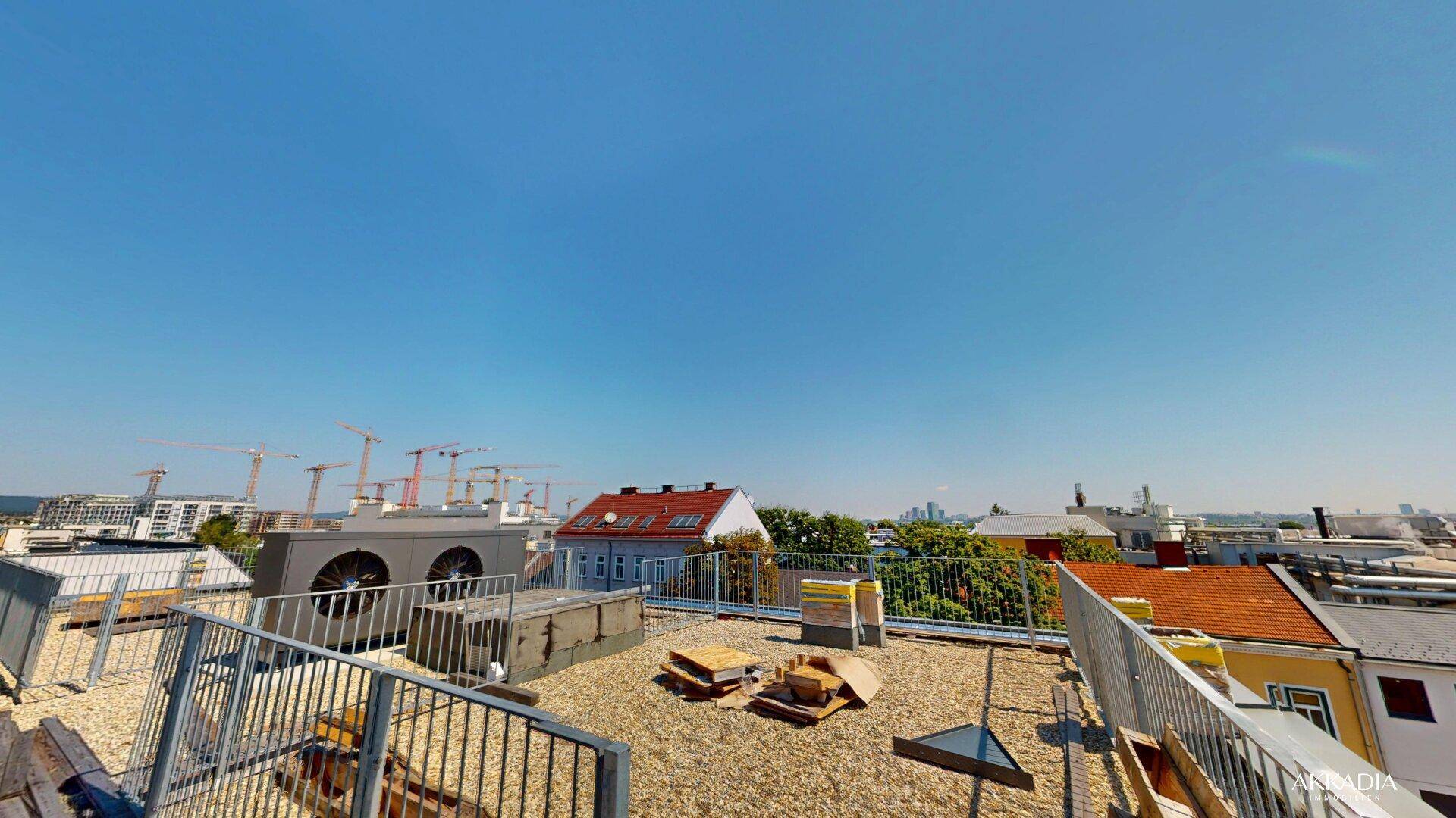 Dachfläche mit Kiesbelag und Blick auf die Stadt mit Baukränen am Horizont.