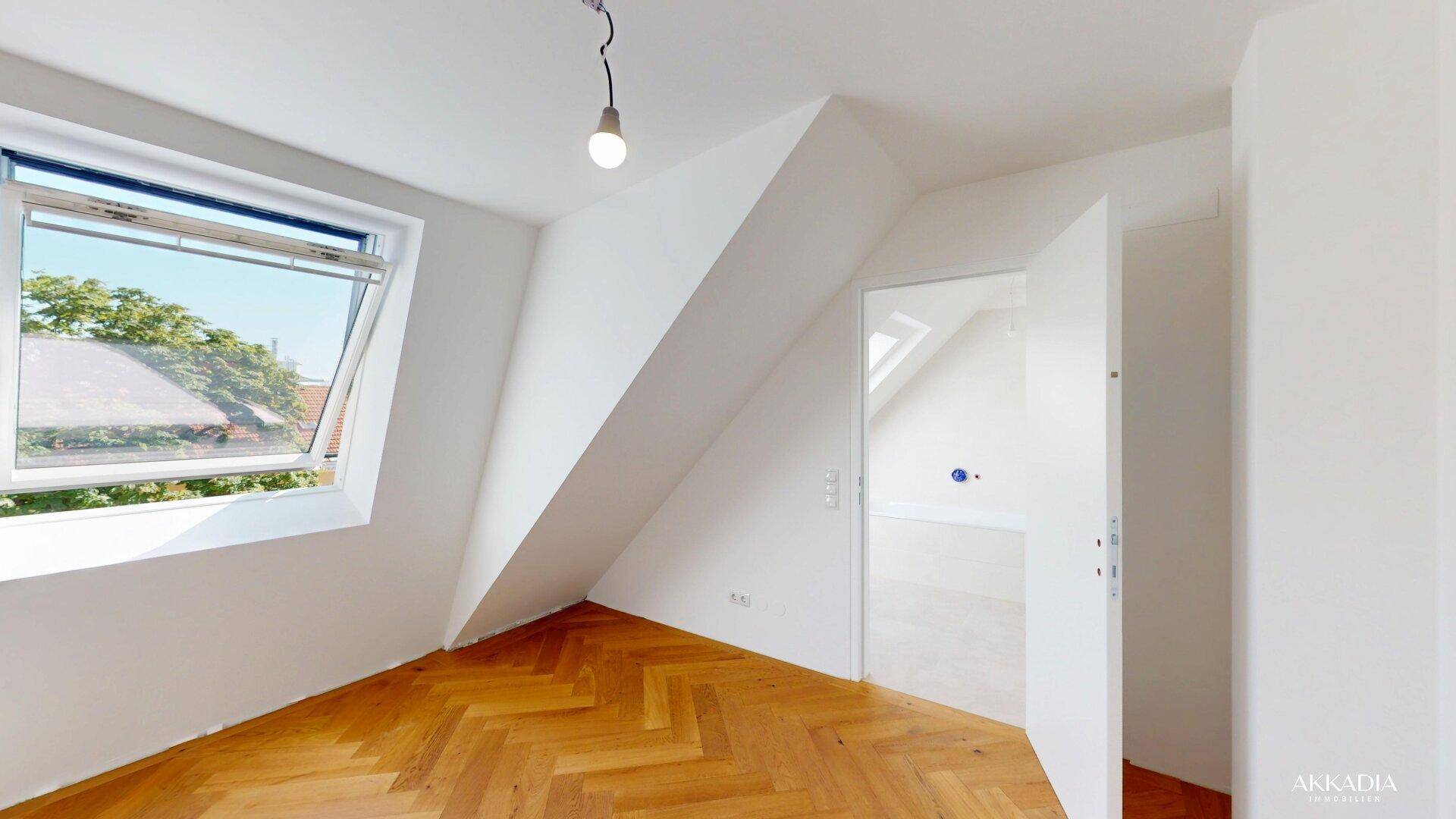 Helles Zimmer mit Dachschräge, Fischgrätparkett und einem großen Dachfenster für viel Tageslicht.