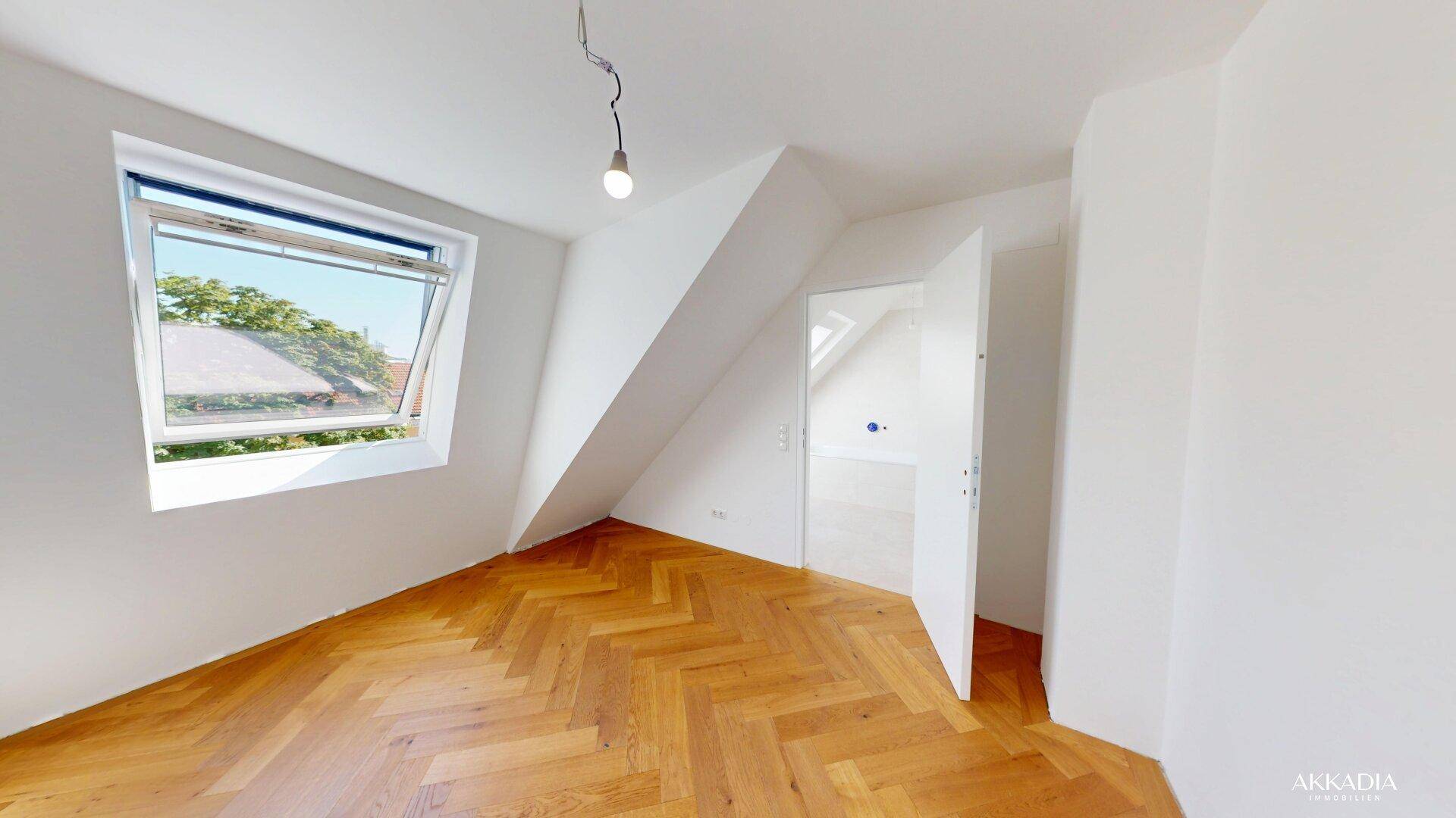 Helles Dachzimmer mit schrägen Wänden, großem Dachfenster und klassischem Fischgrätparkettboden.