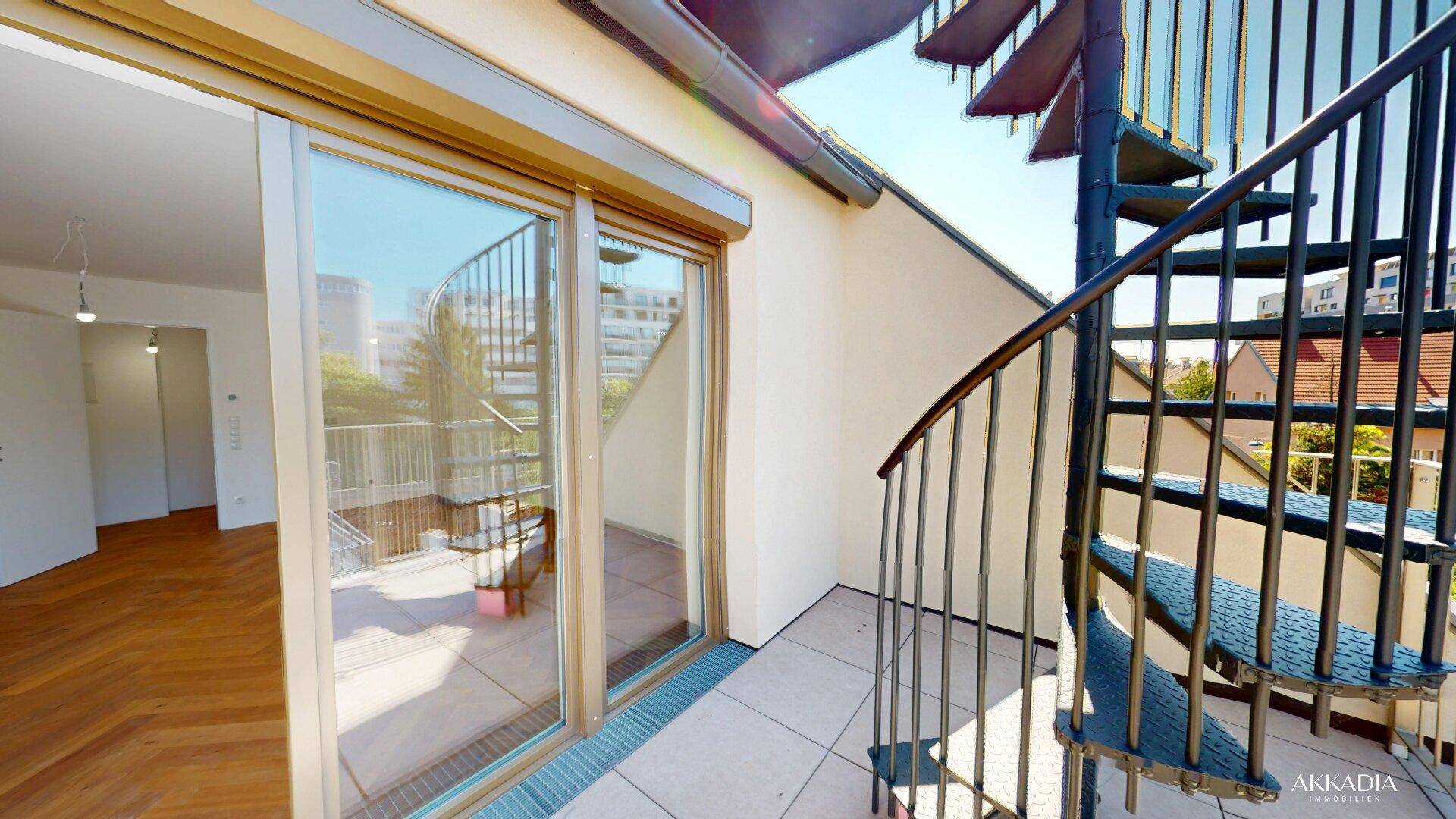 Sonniger Terrassenbereich mit Wendeltreppe und großen Glasfronten, die den Übergang zum Innenraum schaffen.