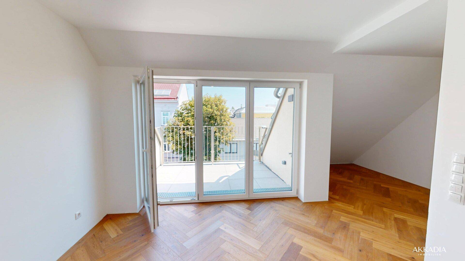 Geräumiger, heller Raum mit Fischgrätparkett und direktem Zugang zu einem Balkon.
