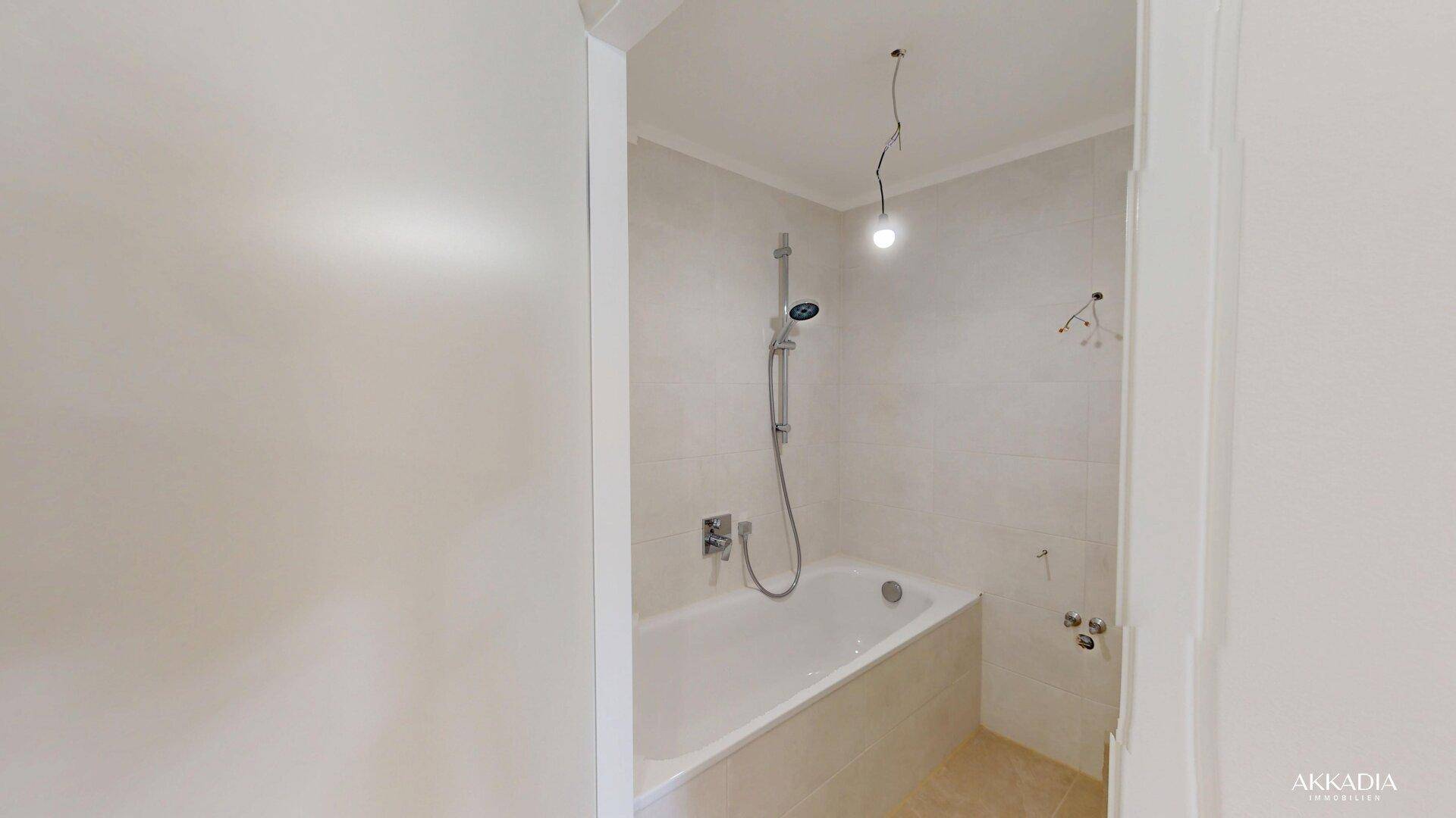 Helles Badezimmer mit eingebauter Badewanne und Duschvorrichtung, komplett mit hellen Fliesen ausgestattet.
