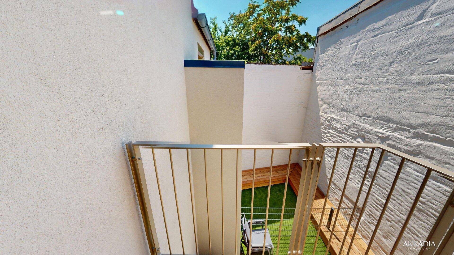 Kleiner, privater Außenbereich mit Kunstrasen und Holzelementen, umgeben von hohen Wänden.