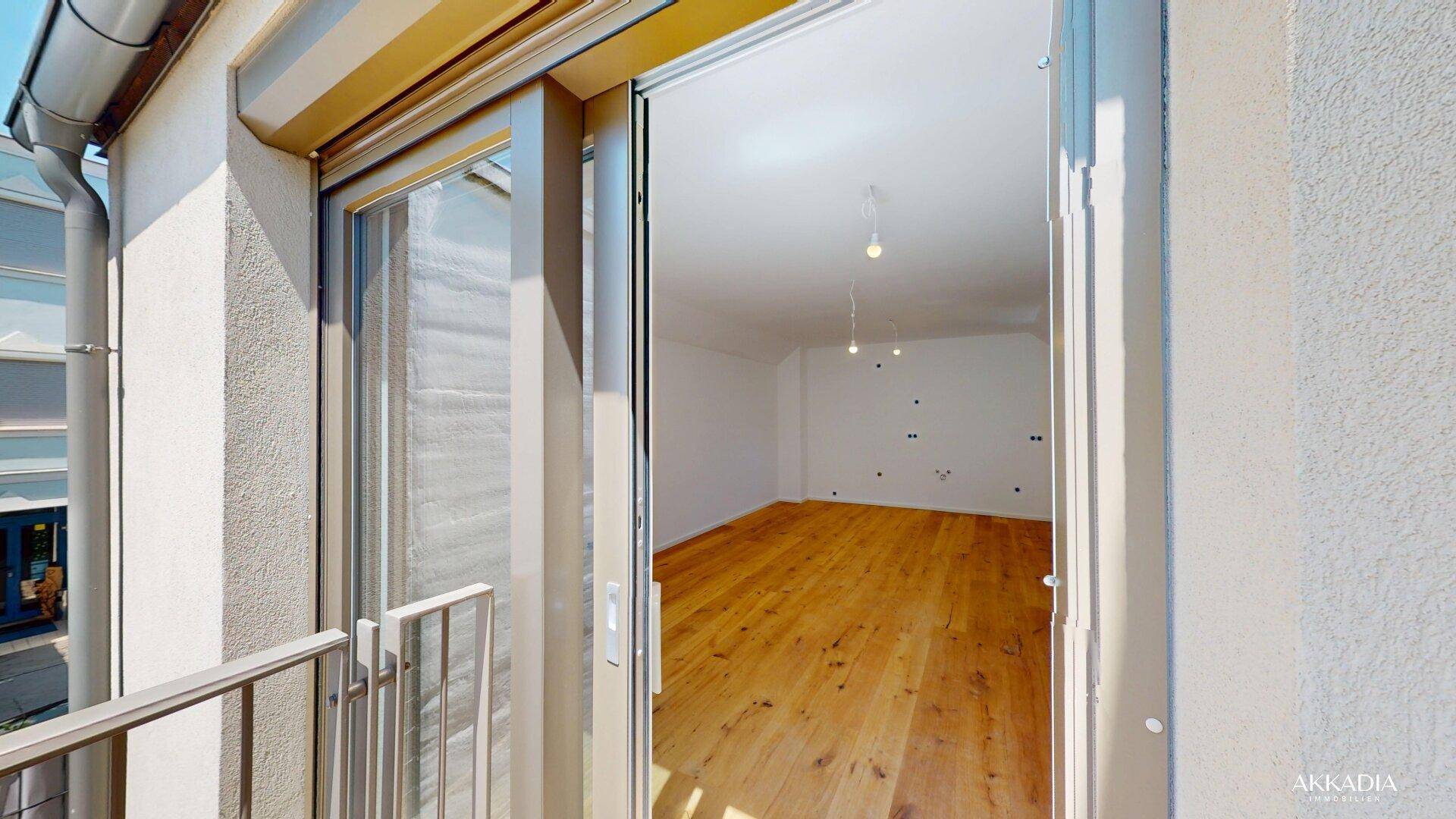 Blick von außen in einen hellen Innenraum mit Holzparkettboden und moderner Ausstattung.