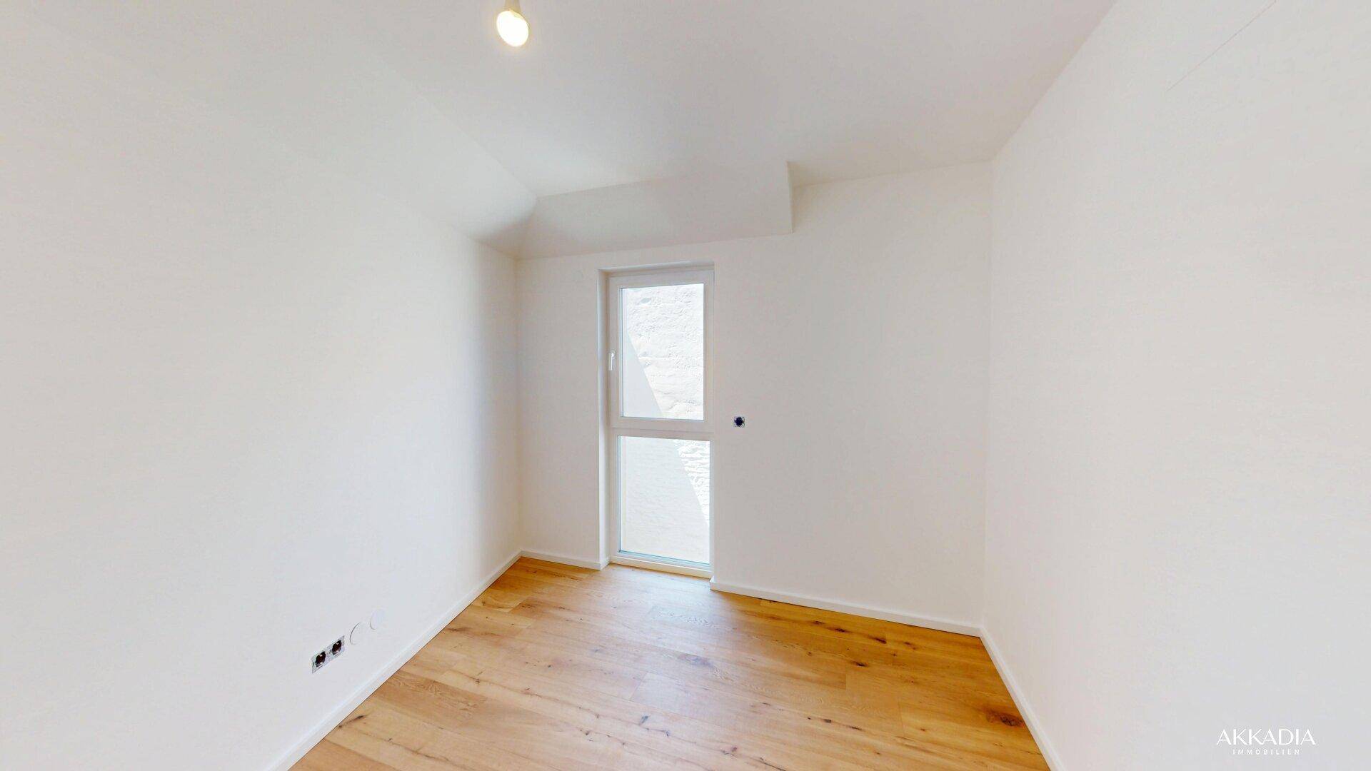 Helles Zimmer mit Holzparkettboden und Zugang zu einem kleinen Außenbereich, ideal als Schlafzimmer.