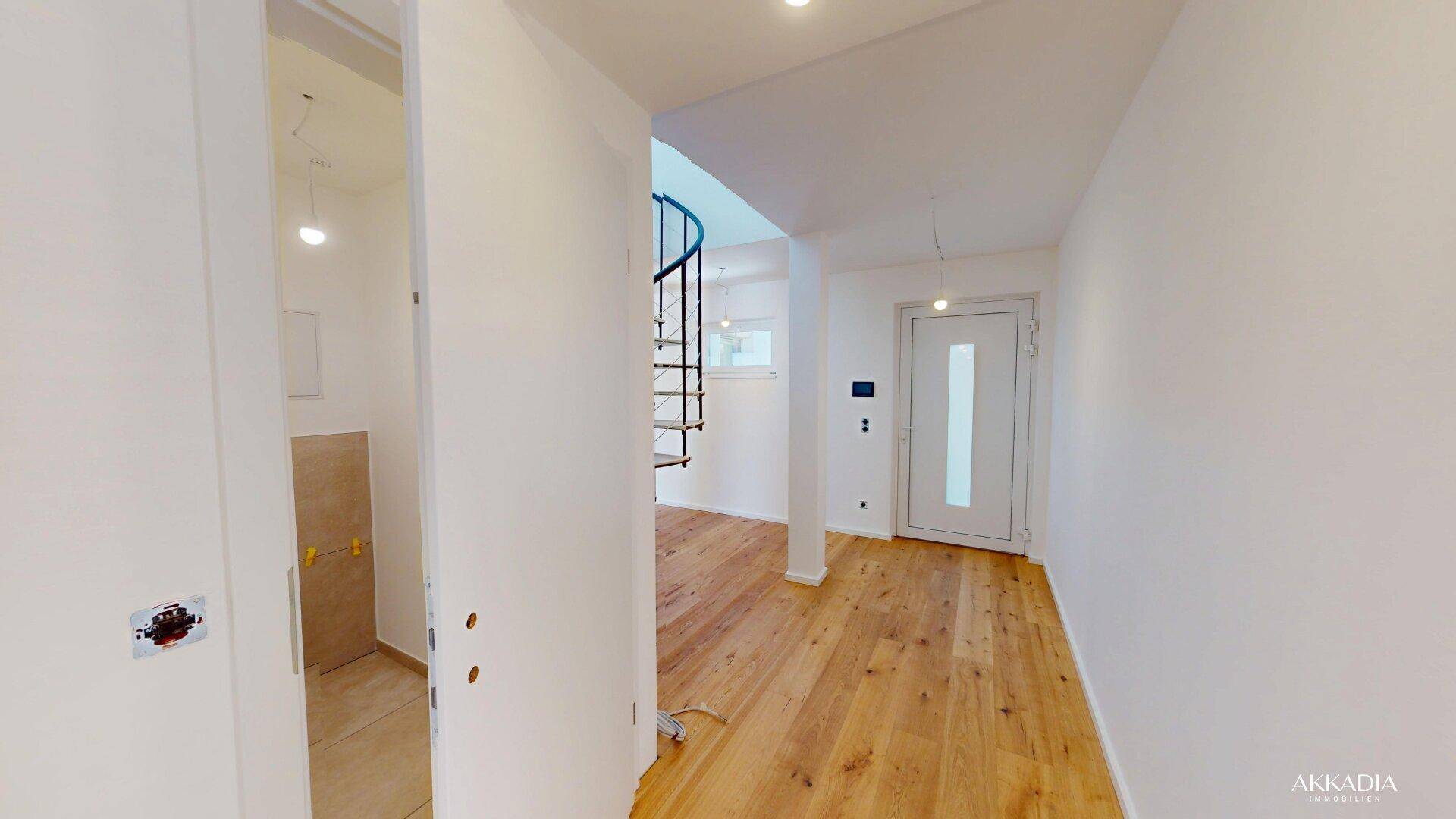 Eingangsbereich mit heller Holzboden und Blick auf die moderne Wendeltreppe und weitere Räume.