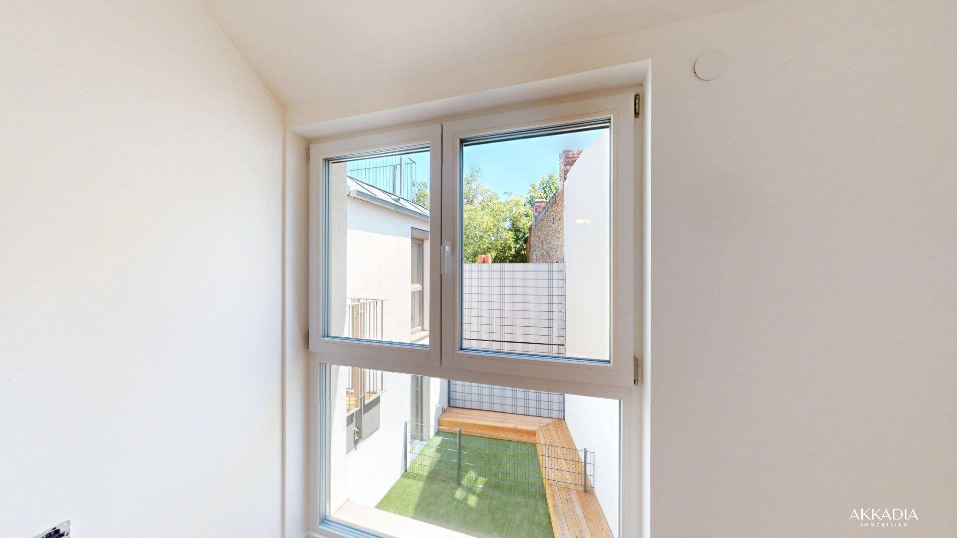 Fenster mit Blick auf einen kleinen Innenhof mit Kunstrasen und Holzelementen.