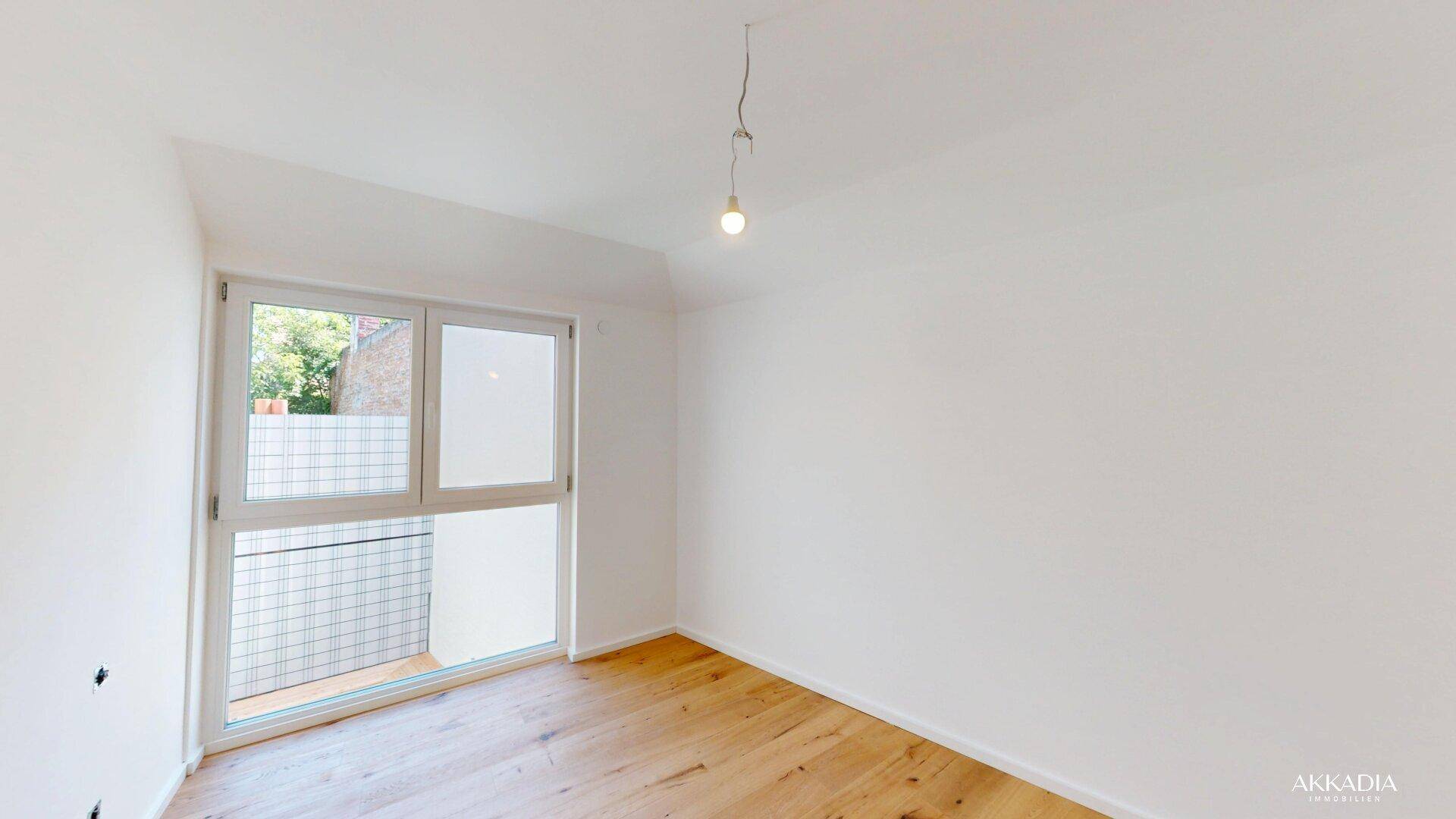 Helles Zimmer mit Holzparkettboden und großem Fenster, das viel Tageslicht hereinlässt.