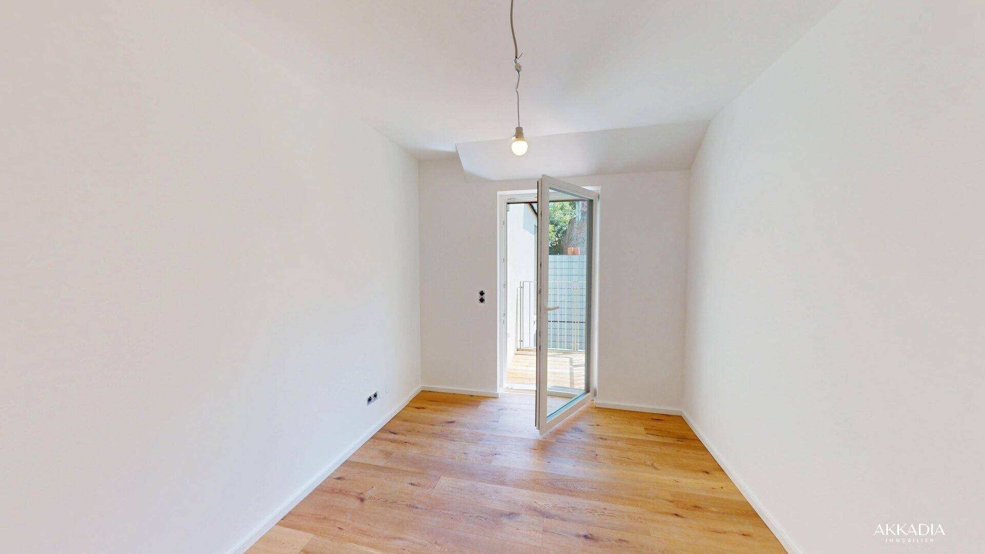 Helles Zimmer mit Holzparkettboden und offener Tür zu einem kleinen Außenbereich.