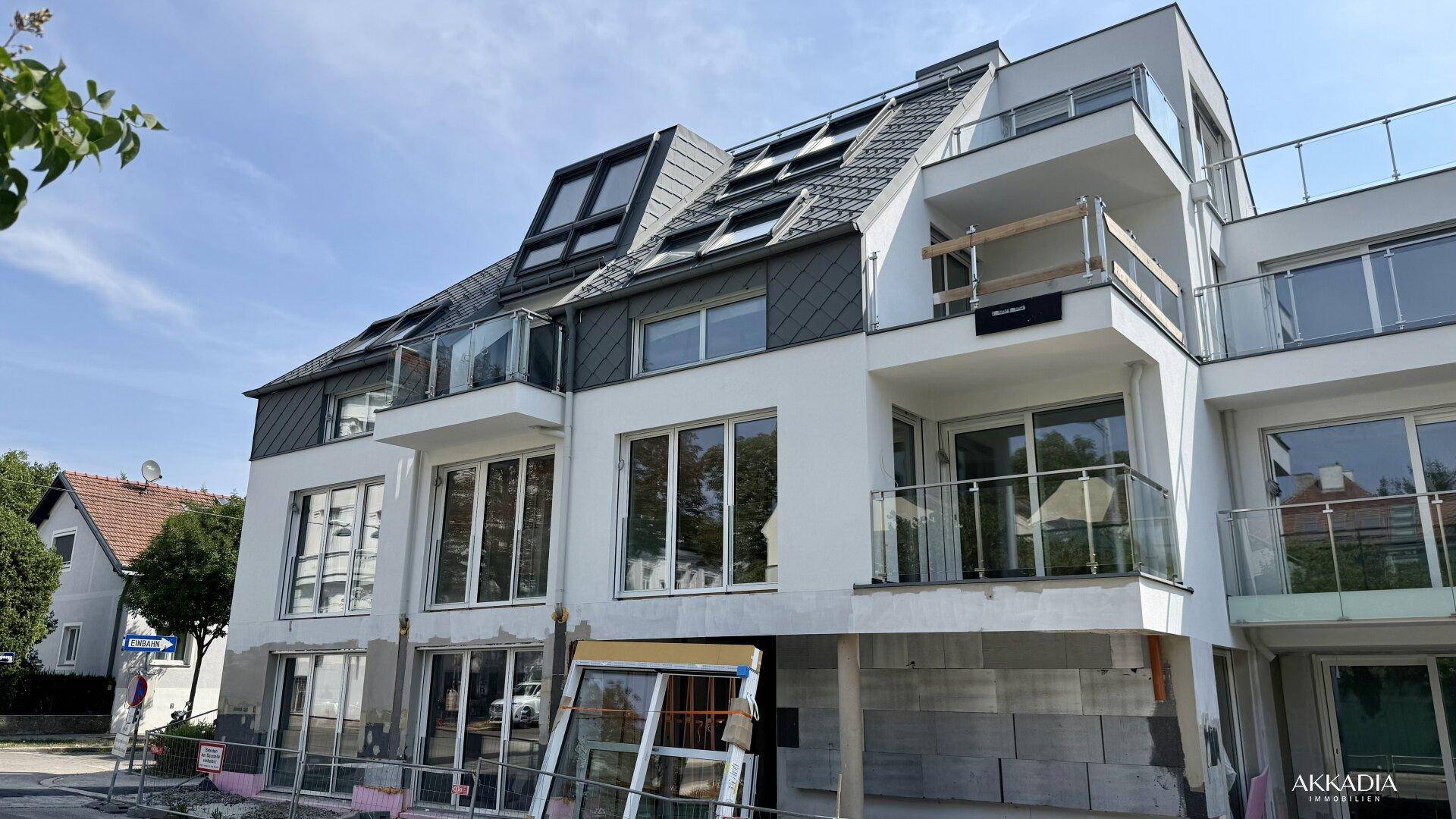 Neubau mit moderner Architektur, Mansarddach, Balkonen und großen Fensterfronten.