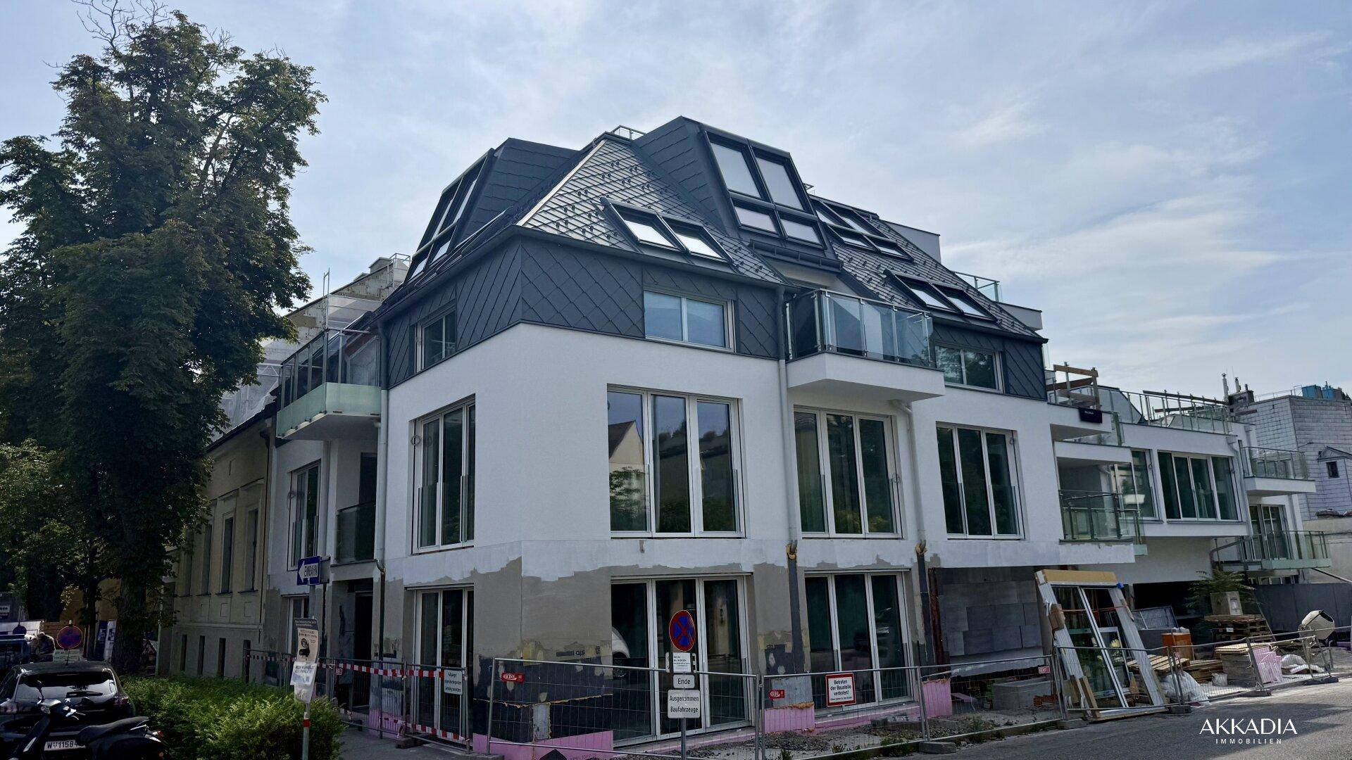 Modernes Wohnhaus im Bau mit dunklem Mansarddach, großen Fenstern und Balkonen.