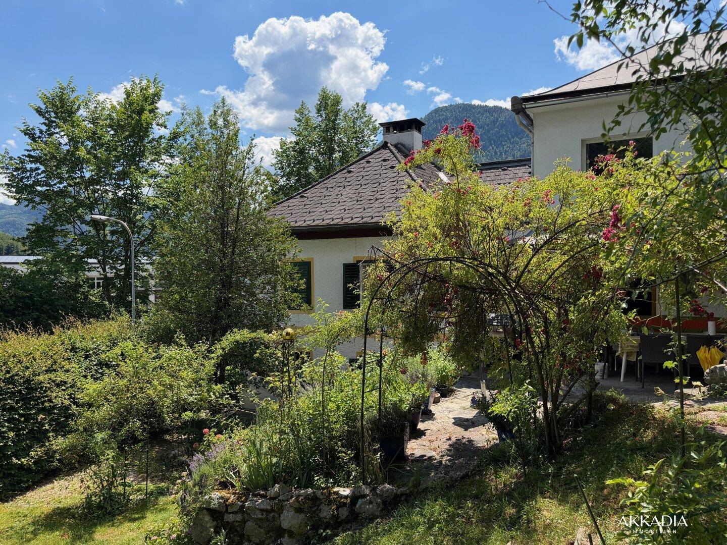 Charmantes Haus mit üppigem Garten, blühenden Pflanzen und Bergblick.