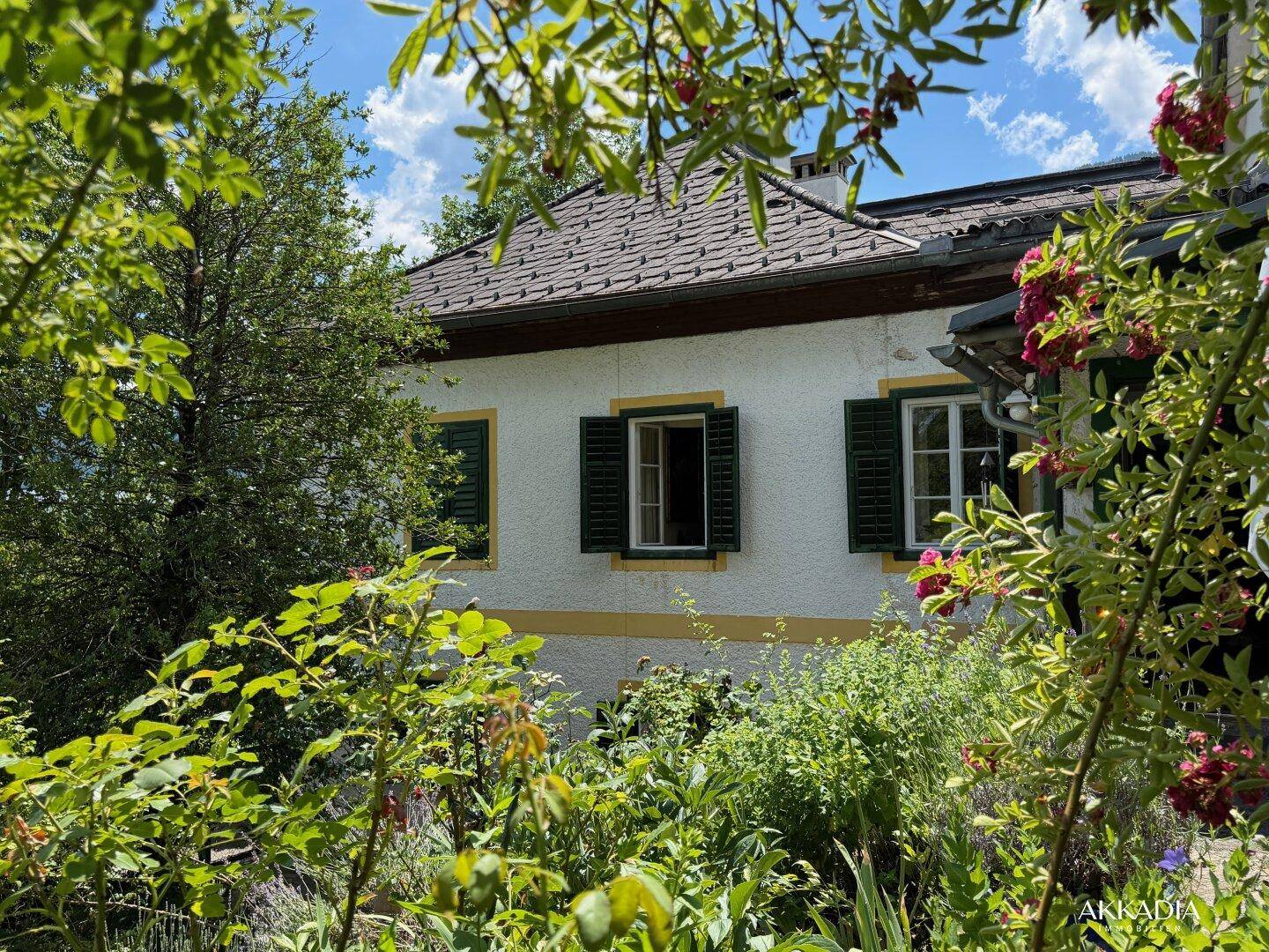 Historisches Haus mit grünen Fensterläden, umgeben von einem blühenden Garten.