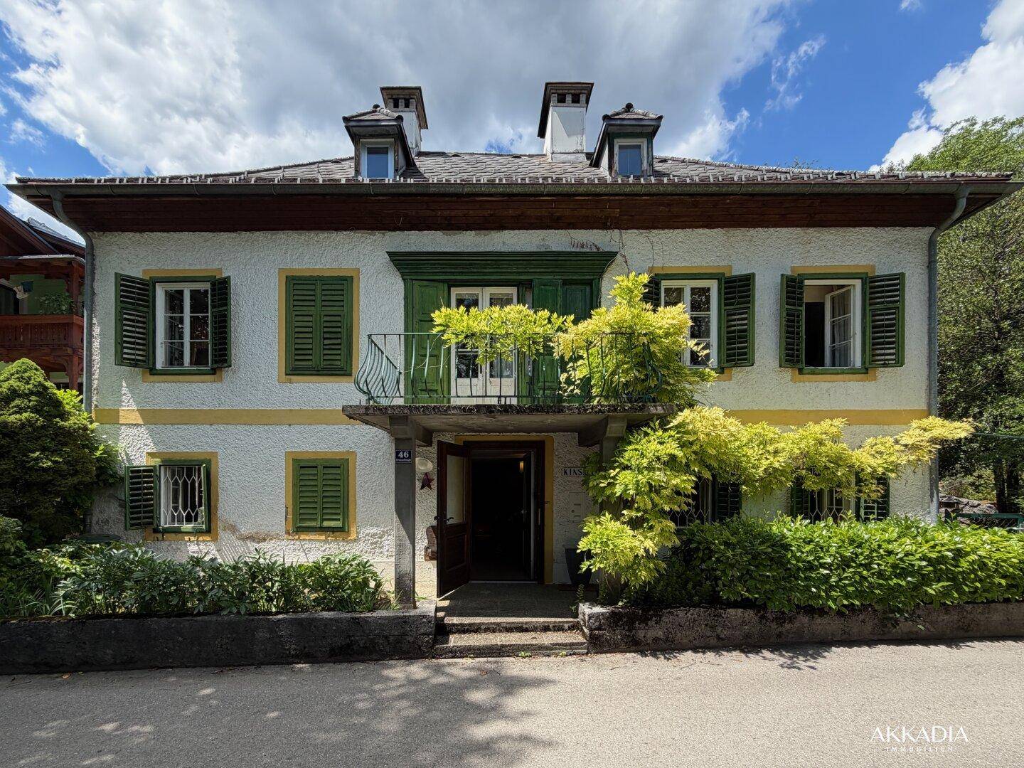 Repräsentative Fassade des Hauses mit Balkon, grünen Fensterläden und Eingangsbereich.