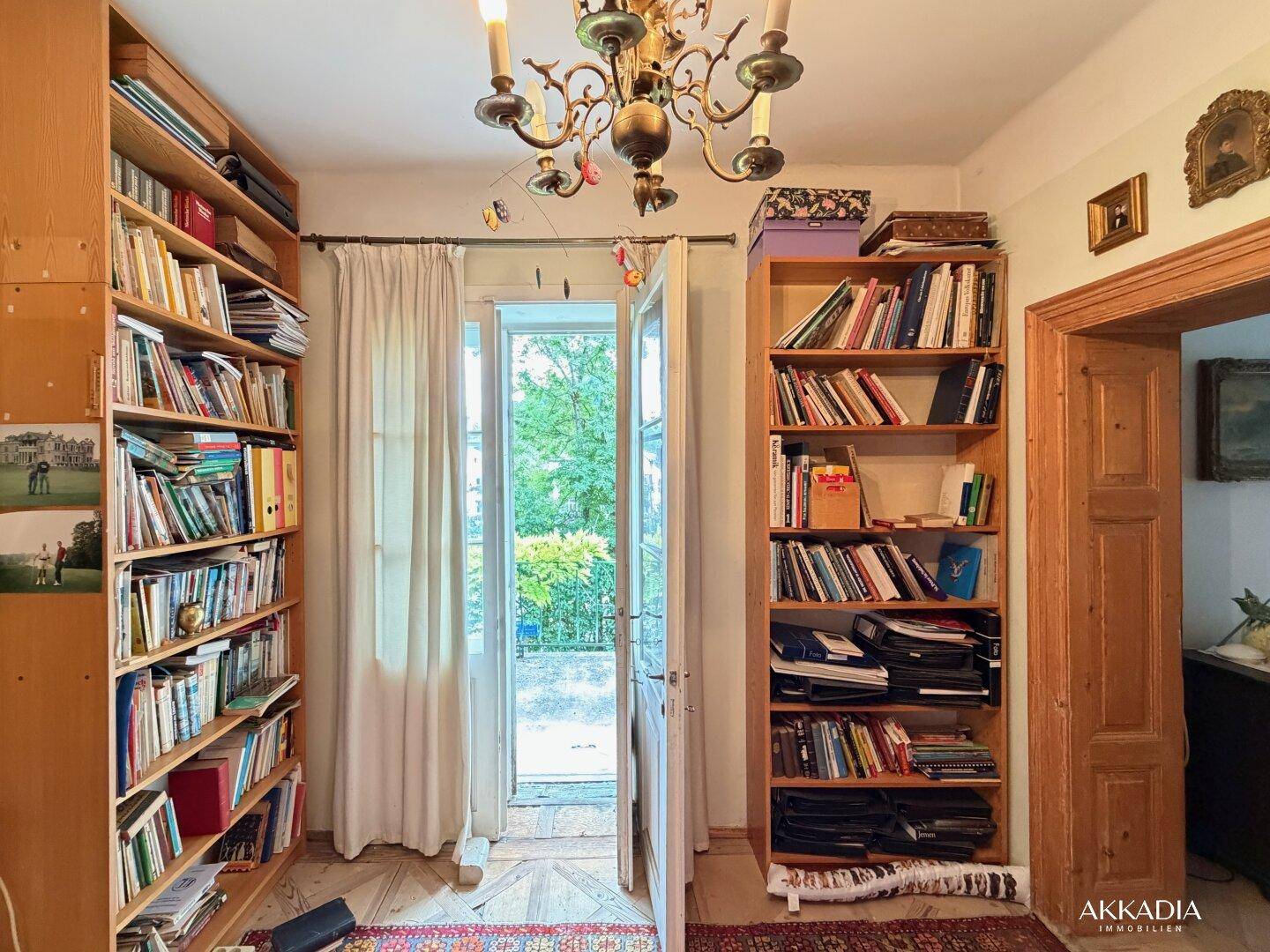 Gemütliches Arbeitszimmer mit Bücherregalen, Holzboden und Zugang zum Balkon.